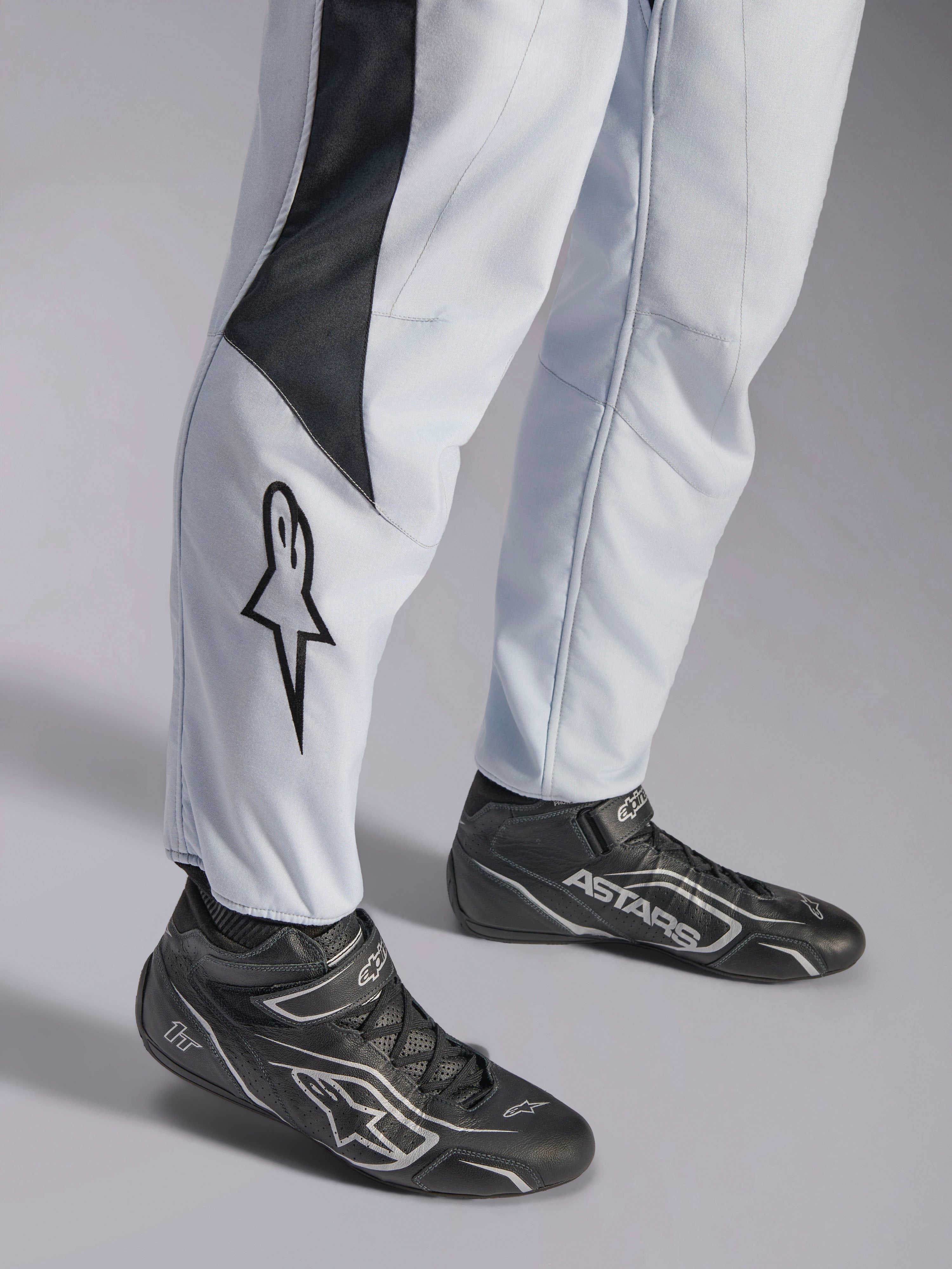 Alpinestars GP Pro Comp V2 FIA racingoverall, grå och svart med stjärnlogotyp på benet och matchande svarta racingstövlar.