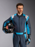 Alpinestars GP Pro Comp V2 racingoverall, FIA-godkänd tävlingsoverall för bilracing, herr, grå och blå med vita detaljer, bärs av en man som håller en kolfiberhjälm.
