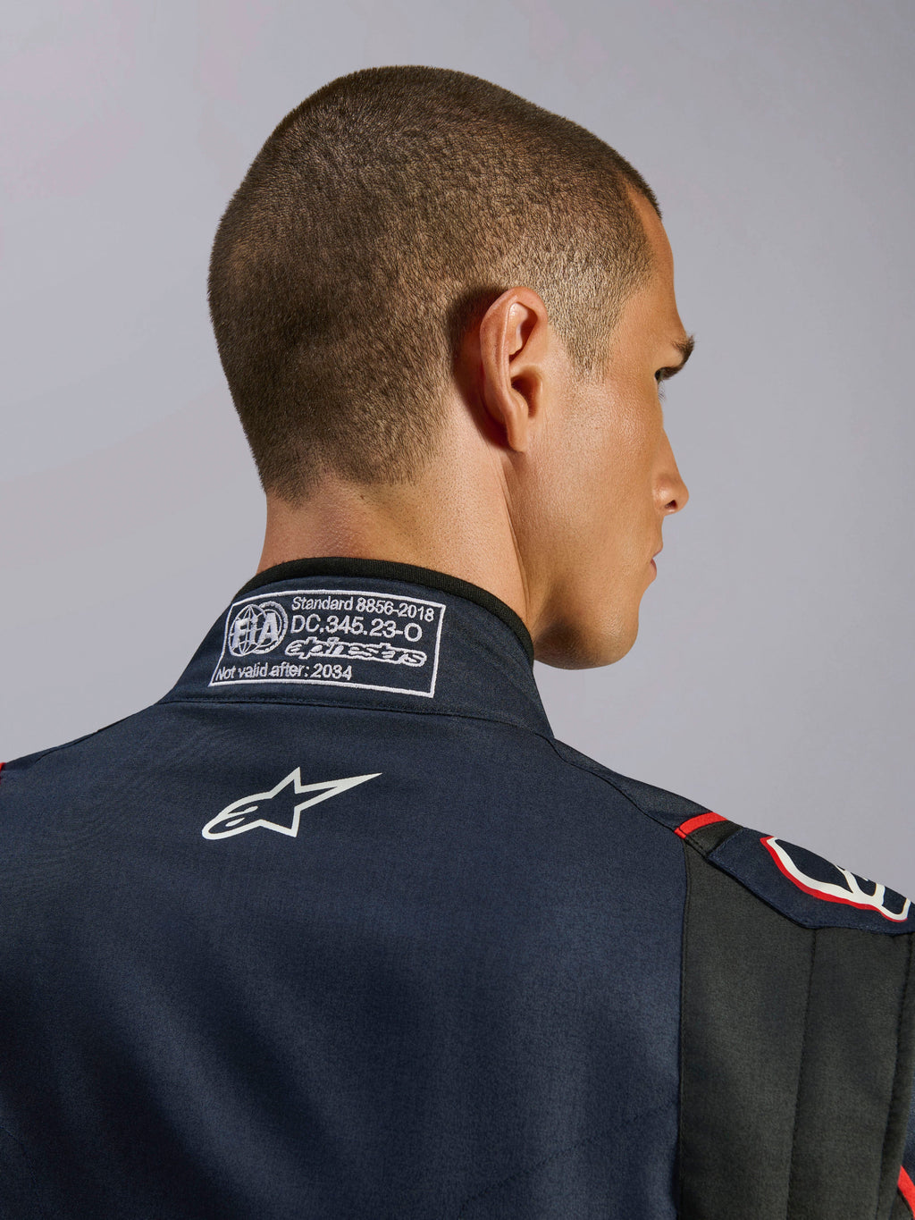 Alpinestars GP Tech V4-overall i marinblått, svart och rött, närbild på kragen baktill med FIA 8856-2018-certifieringsetikett och vit broderad Alpinestars-logotyp, detalj av högpresterande racingoverall
