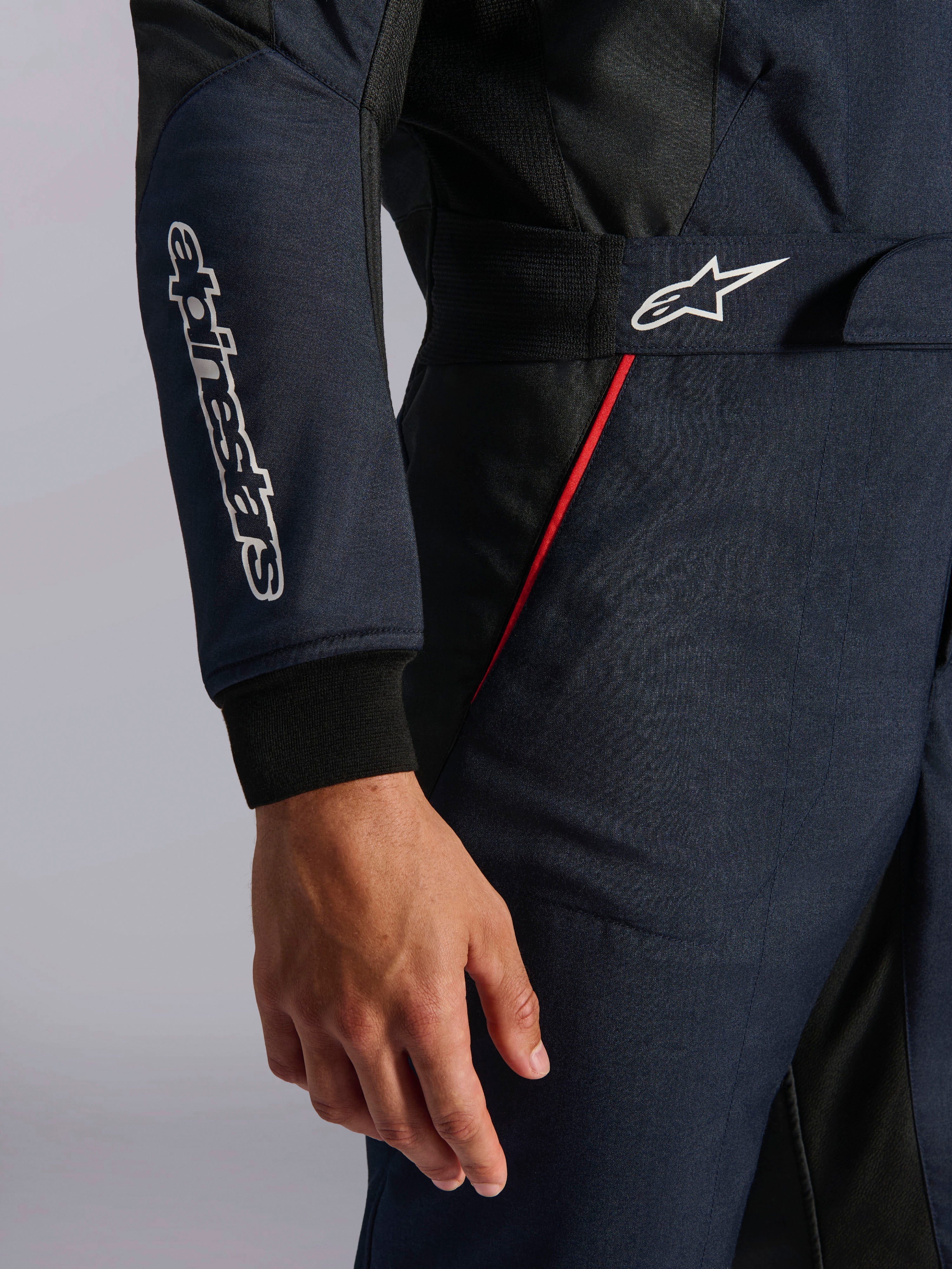 Alpinestars GP Tech V4-dräkt i marinblått, svart och rött, detaljbild av midjan och ärmen med vita Alpinestars-logotyper, röda accentpasspoaler och texturerat twilltyg.