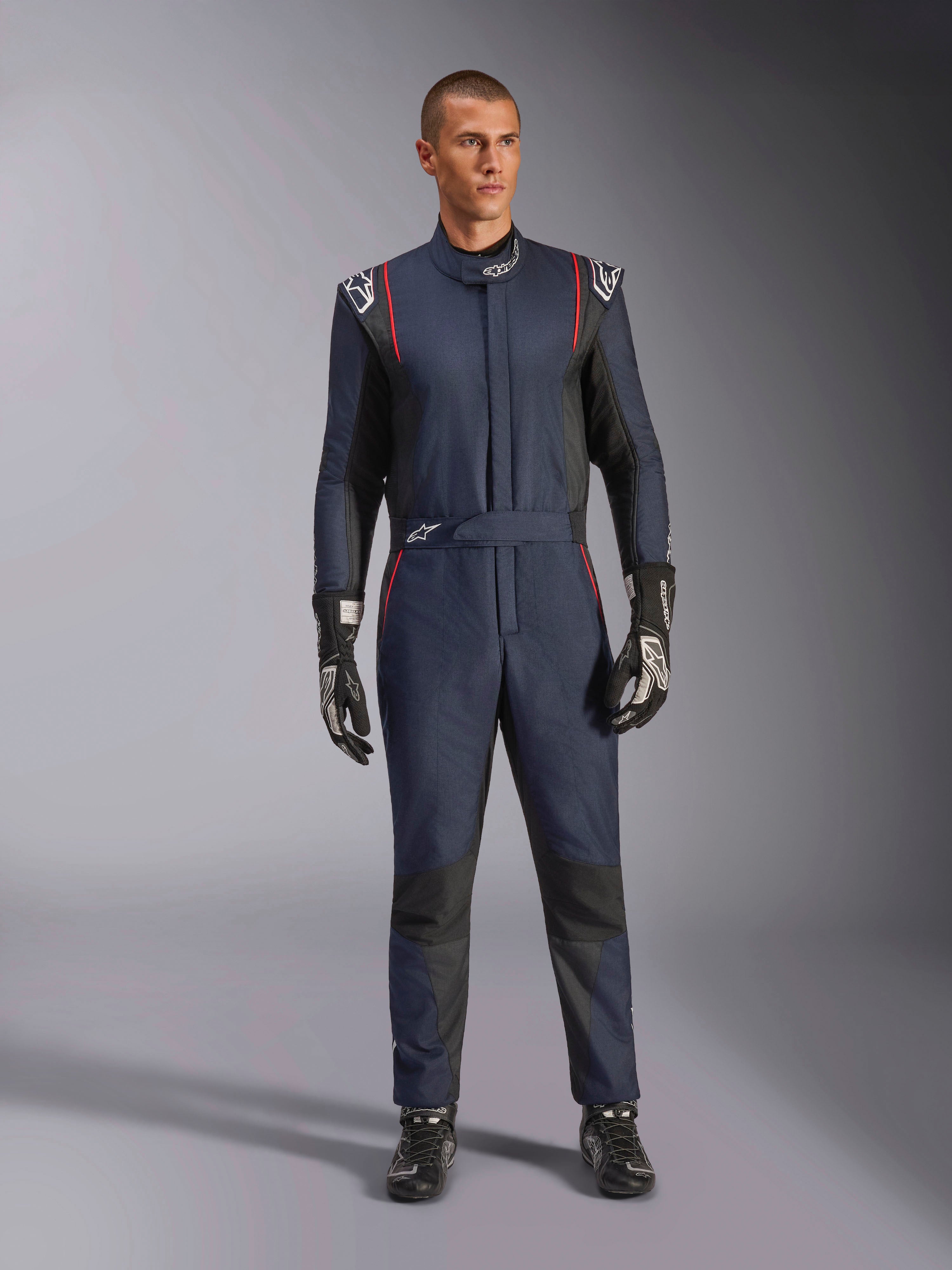 Alpinestars GP Tech V4 Suit, professionell racingoverall i marinblått och svart med röda detaljer, FIA-certifierad racingutrustning i ett stycke, bärs med svarta racinghandskar och skor, förarutrustning för motorsport