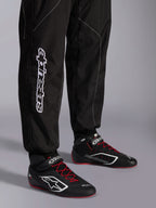 Alpinestars KMX-9 V3-dräkt, kartingdräkt, svart och vit, vy över underbenen som visar stor vit Alpinestars-logotyp, bärs med svarta och röda racingskor, professionell motorsportutrustning för karting