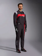 Manlig modell bär Alpinestars KMX-9 V3 Graphic 3-dräkt, kartingdräkt, svart och röd, med vita axelepåletter och röd logotyp på bröstet, kombinerat med svarta racinghandskar och skor med röda skosnören, professionell motorsportutrustning.