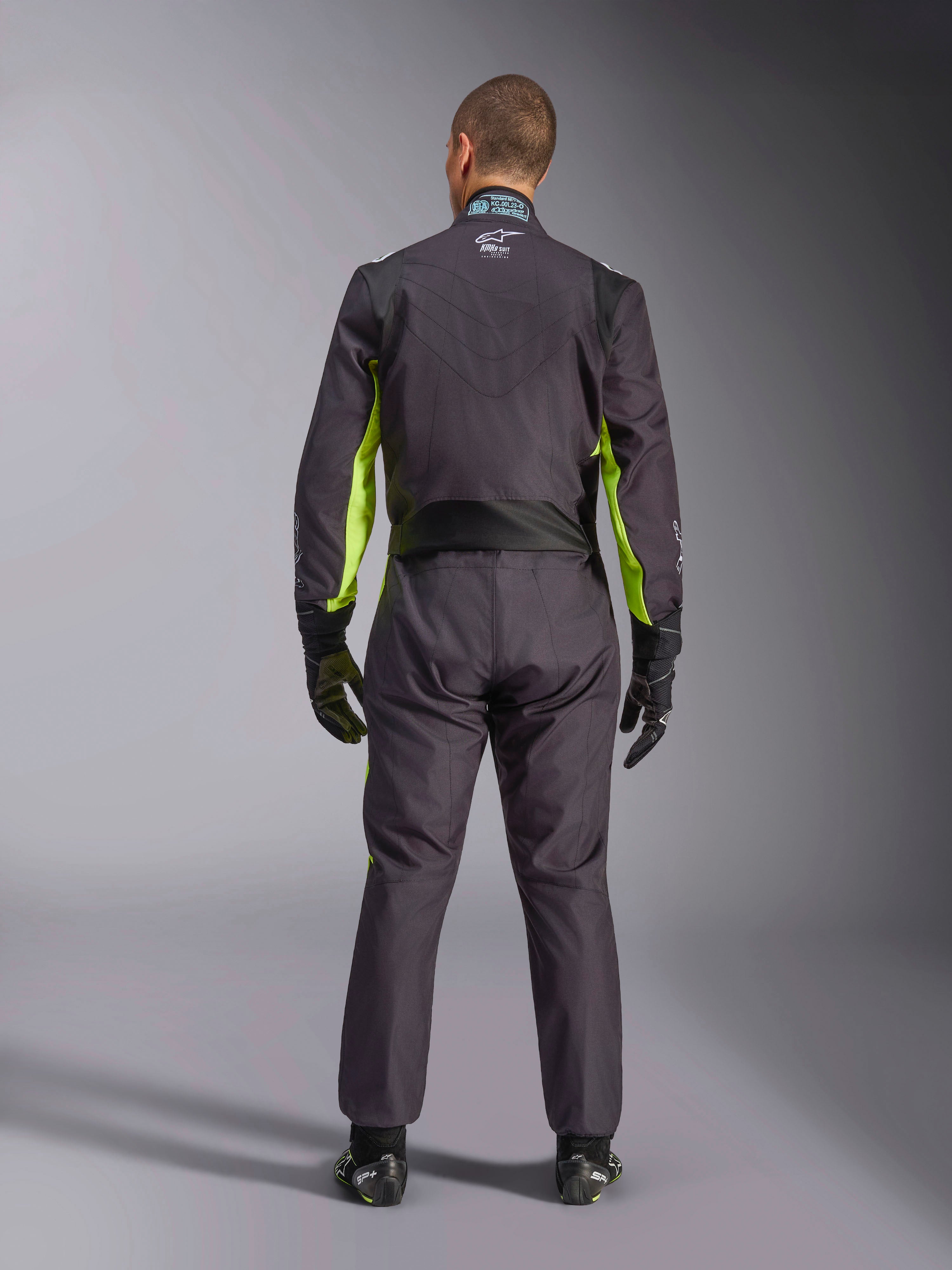 Helbild bakifrån av en person som bär Alpinestars KMX-9 V3 Graphic 3 Suit, kartingoverall i svart och fluorescerande gult, som visar ergonomiska stretchpaneler på ryggen och axlarna, matchad med svarta racinghandskar och skor.