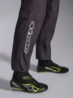 Alpinestars KMX-9 V3 Graphic 3-dräkt, kartingoverall, svart, närbild på underbenen och ankelmuddarna med vit vertikal Alpinestars-branding, kombinerad med svarta och neongula kartingskor, detalj av professionell kartingutrustning