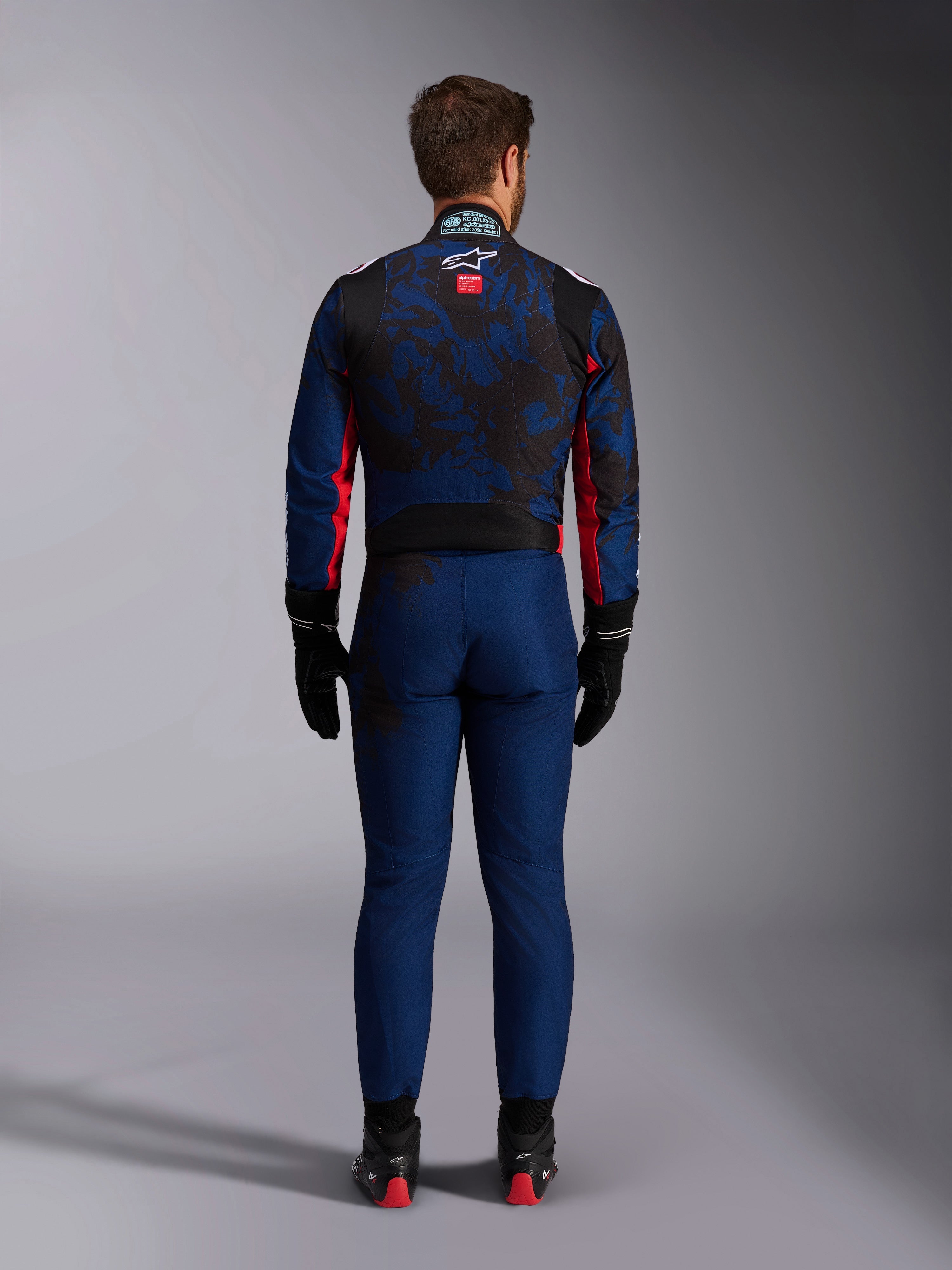 Kartingförare sedd bakifrån iförd KMX-9 V3 Graphic 5 Suit i Navy Red, med ett marinblått och svart grafiskt mönster, röda sidodetaljer och Alpinestars-logotypen på övre delen av ryggen, kombinerat med svarta racinghandskar och skor.