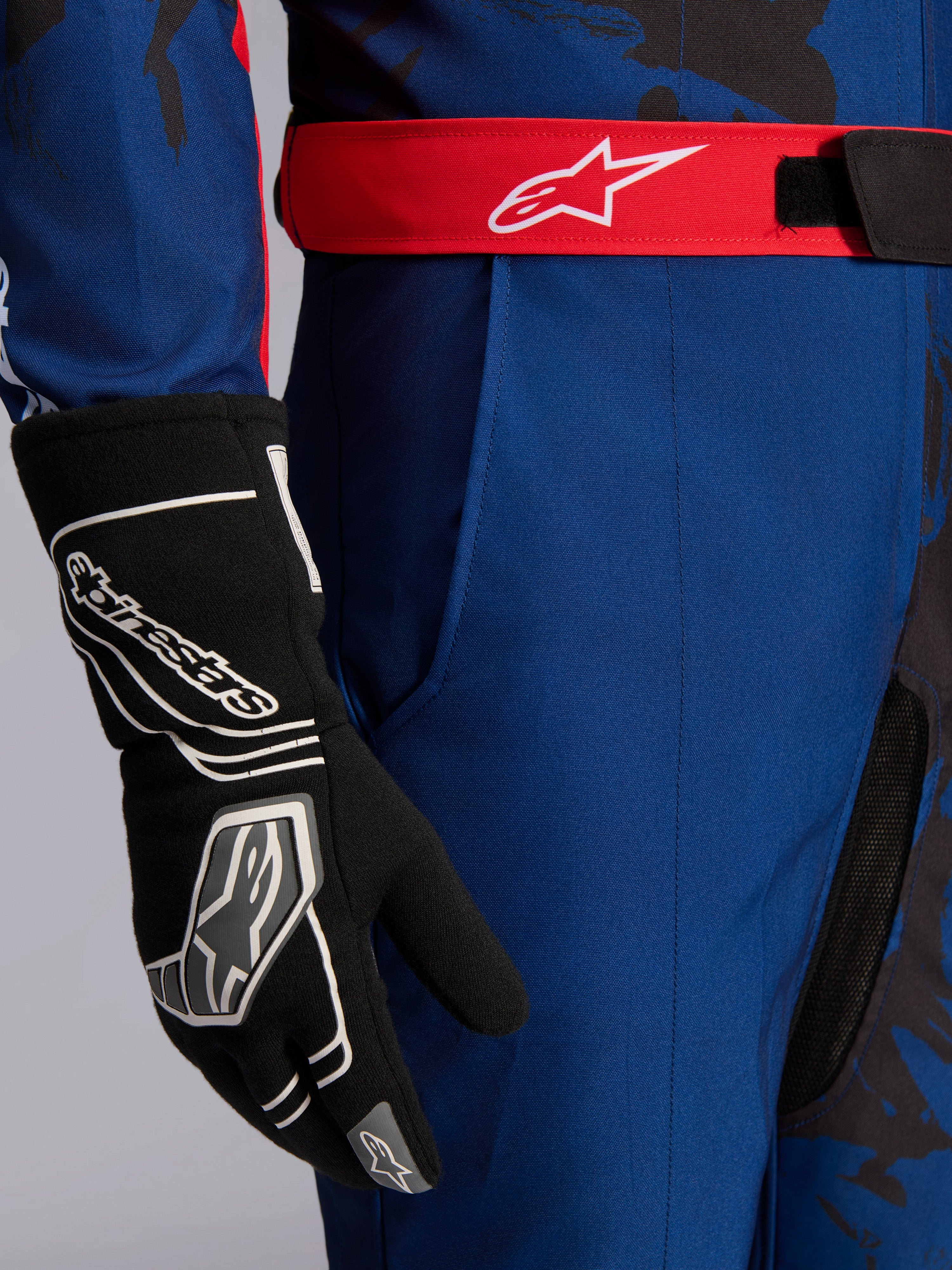 Alpinestars KMX-9 V3 Graphic 5 kartingoverall, marinblå och röd, närbild som visar rött justerbart midjebälte med vit logotyp, bärs med svart kartinghandske, hållbart marinblått tyg och integrerad lårficka