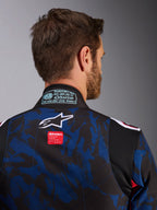 Närbild av Alpinestars KMX-9 V3 Graphic 5-overall, kartingoverall i Navy Red, med blått och svart kamouflagemönster, vit stjärnlogotyp och röd märkesetikett på övre ryggen, FIA 8877-2022-certifieringsmärke på kragen
