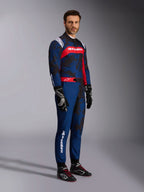 Modell som bär Alpinestars KMX-9 V3 Graphic 5 Suit i Navy Red, helkroppsbild inklusive svarta kartinghandskar och svarta racingskor, marinblå dräkt med mörk grafik i kamouflagestil och en framträdande röd bröstpanel med vit logotyp, professionell skyddsutrustning för karting
