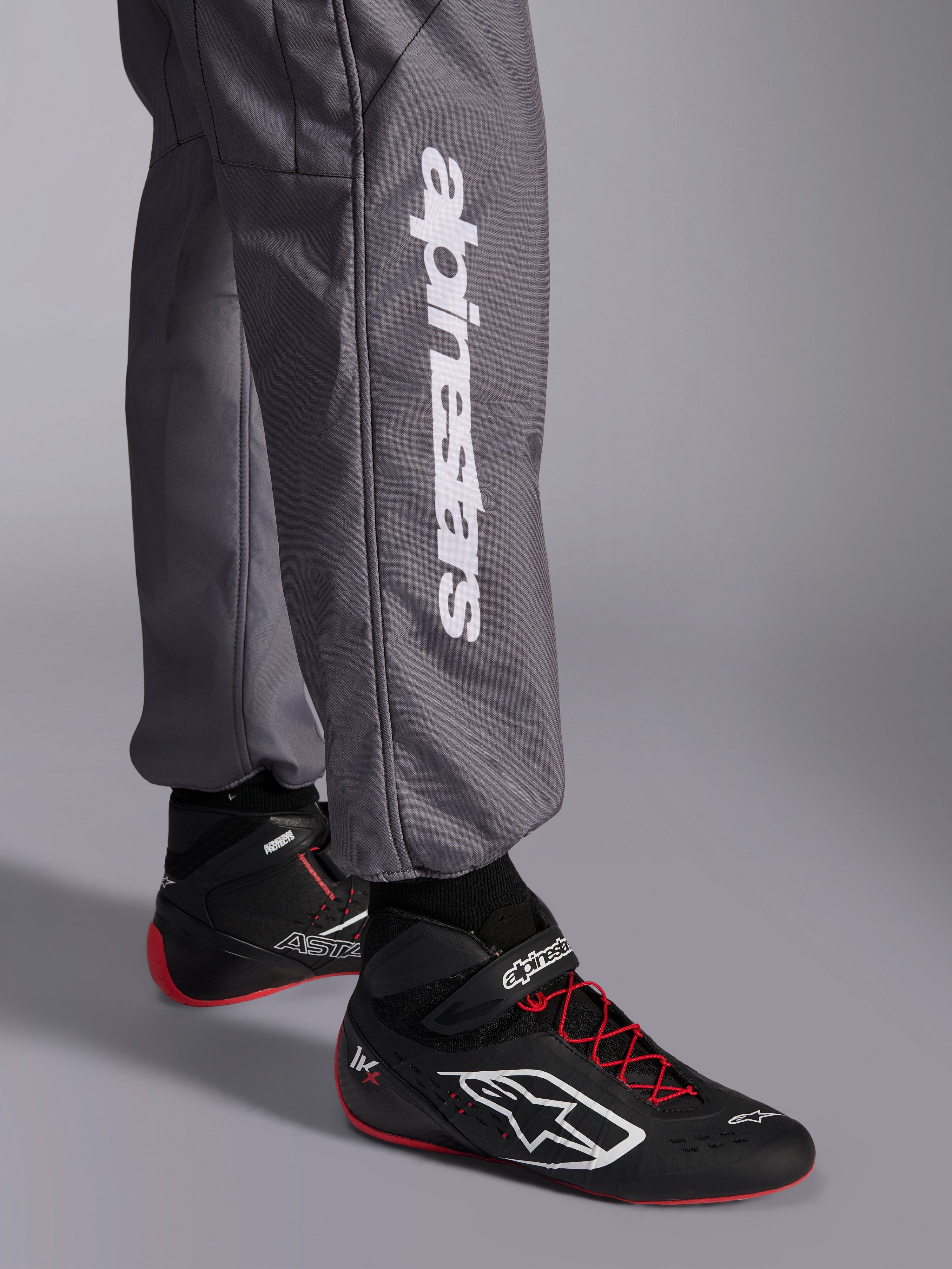 Alpinestars KMX-9 V3 Graphic 5 Suit, Karting Suit, Dark Gray, close-up of lower leg featuring white vertical Alpinestars logo, worn with black and red racing shoes, durable material for karting competition
