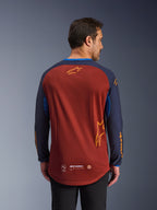 Alpinestars Maxdura Dual Jersey i Rust Brown och Mood Indigo, sedd bakifrån, med en ventilerande mesh-torso, mörkblå ärmar med orange Alpinestars-logotyp och ett förlängt bakstycke för extra täckning.