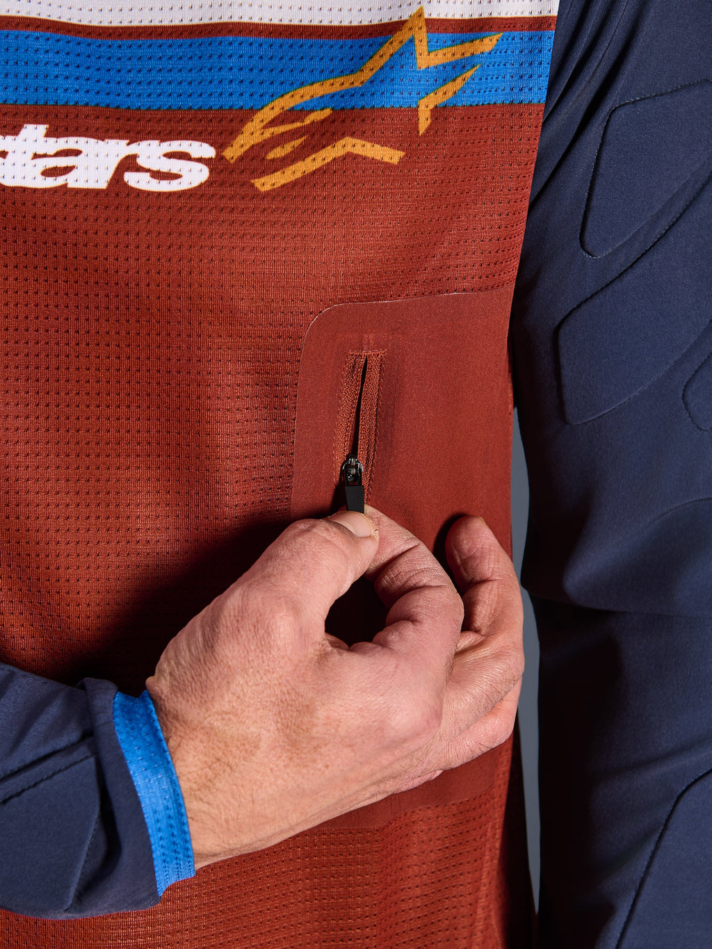Närbild av Alpinestars Maxdura Dual Jersey, rostbrun mesh-torso med sömlös bröstficka med dragkedja, Mood Indigo-ärmar med integrerad vaddering, teknisk detalj på äventyrsmotorcykeltröja