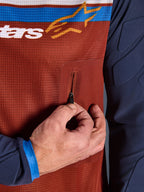 Närbild av Alpinestars Maxdura Dual Jersey, rostbrun mesh-torso med sömlös bröstficka med dragkedja, Mood Indigo-ärmar med integrerad vaddering, teknisk detalj på äventyrsmotorcykeltröja