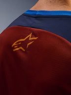 Närbild på Alpinestars Maxdura Dual Jersey, rostbrunt meshtyg på baksidan, liten orange stjärnlogotyp, mörkblå övre panel och klarblå kragkant, detaljerad vy av äventyrsmotorcykeltröja
