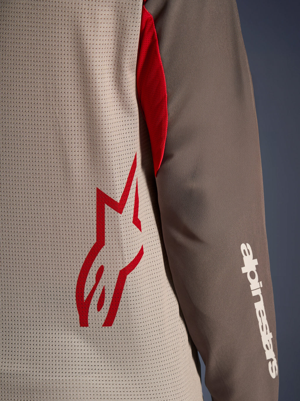 Alpinestars Maxdura Dual Jersey, Aluminum Walnut, närbild som visar den ventilerade torson i mesh med en röd stjärnlogotyp och en brun nötningsbeständig ärm med en vit Alpinestars-text, teknisk adventure- och dual-sport-motorcykelutrustning