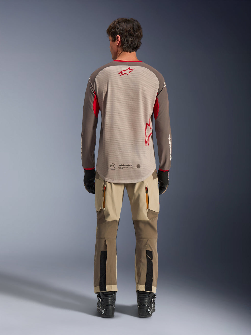 Alpinestars Maxdura Dual Jersey i Aluminum Walnut, sedd bakifrån, beige mesh-torso med bruna ärmar och röda logotyper, förlängt bakstycke, kombinerat med adventure-körbyxor och svarta stövlar.