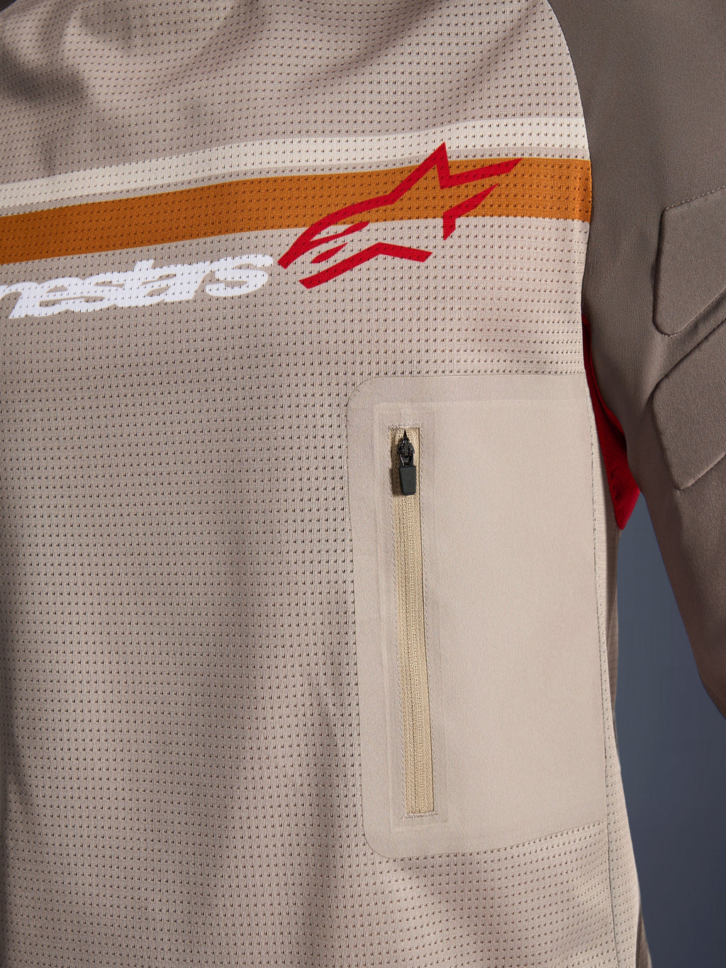 Alpinestars Maxdura Dual Jersey, Aluminum Walnut, närbild på torson i mesh, horisontell orange och vit rand med röd logotyp, vertikal bröstficka med dragkedja, adventure-motorcykelkläder