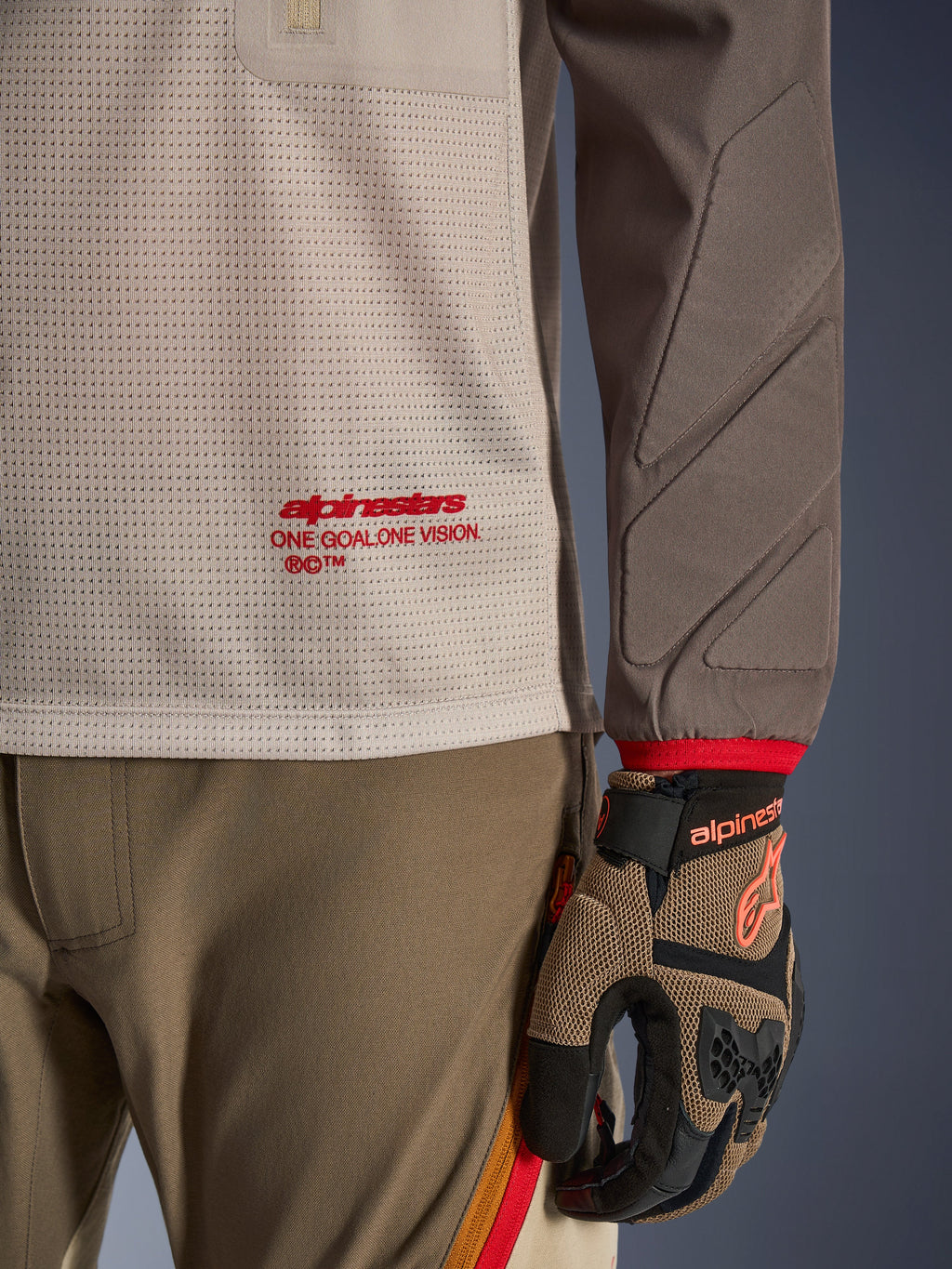 Alpinestars Maxdura Dual Jersey i Aluminum Walnut, detaljvy som visar torson i ventilerad mesh med röd logotyp, nötningsresistent ärm med integrerad vaddering, bärs med matchande adventure-byxor och handskar