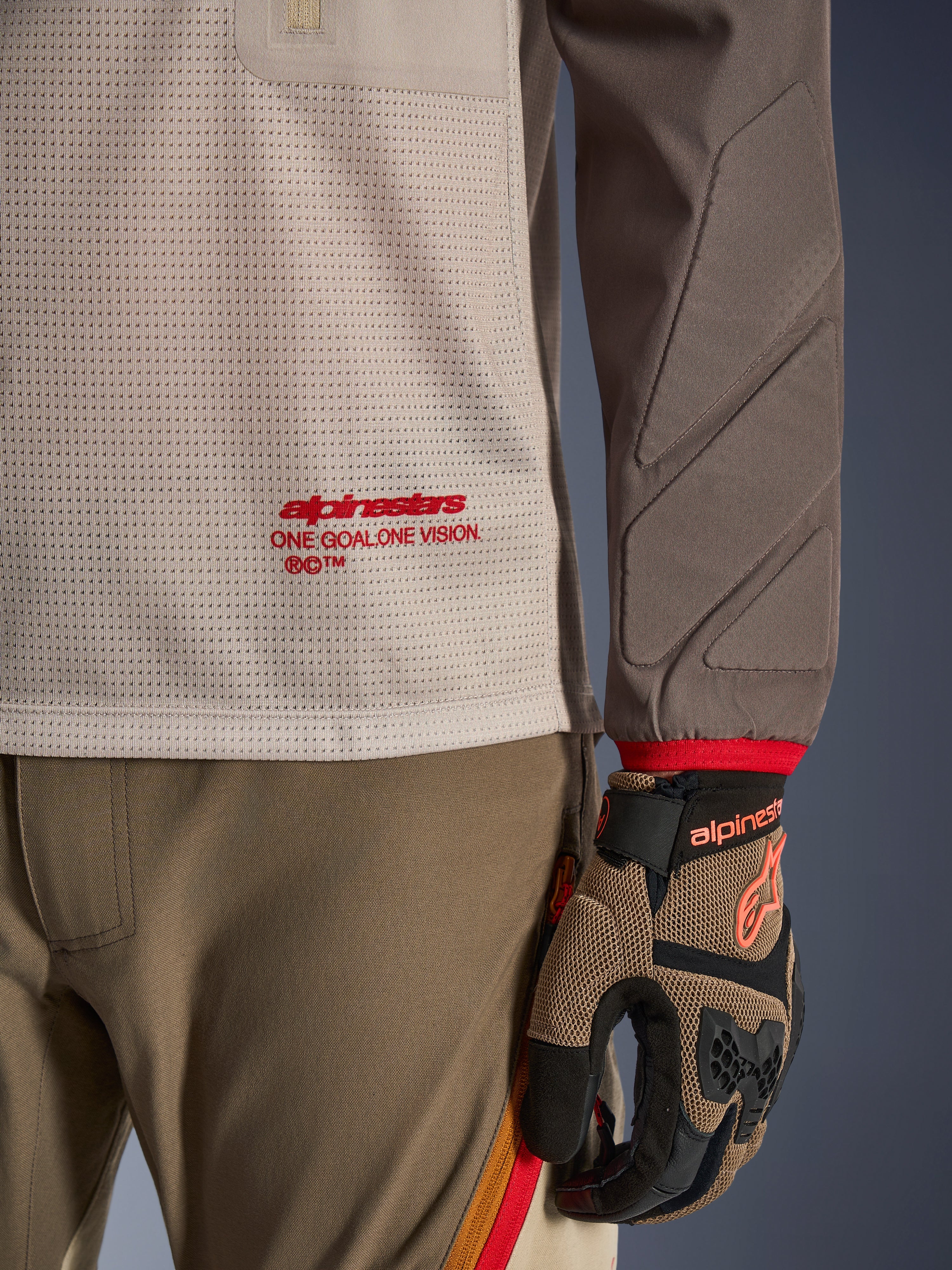 Alpinestars Maxdura Dual Jersey i Aluminum Walnut, detaljvy som visar torson i ventilerad mesh med röd logotyp, nötningsresistent ärm med integrerad vaddering, bärs med matchande adventure-byxor och handskar
