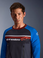 Alpinestars Maxdura Dual Jersey, mörkgrå och kungsblå, bärs av en manlig modell, med bål i mesh, kungsblå ärmar med integrerad vaddering, vertikala bröstfickor med dragkedja och Alpinestars-logotyp över bröstet.