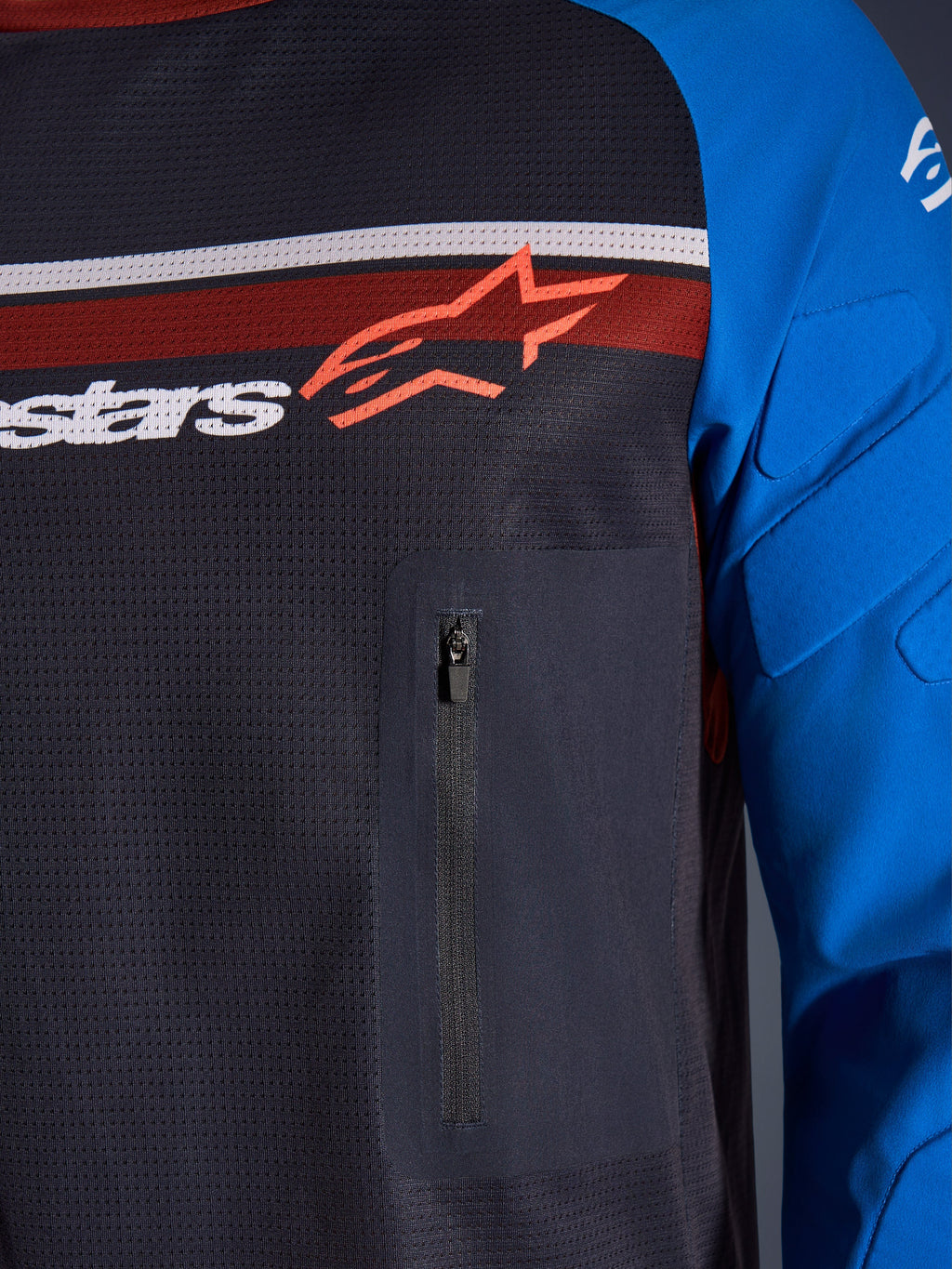 Alpinestars Maxdura Dual Jersey, närbild på bröst och ärm, mörkgrå och kungsblå, med bröstficka med dragkedja, ventilerande mesh-bål och integrerad vaddering på ärmarna, Alpinestars-logotyp över röda och vita ränder