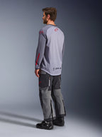 Man som bär Alpinestars Maxdura Dual Jersey, ljusgrå med röda Alpinestars-logotyper, vy bakifrån som visar mesh-torso och långa ärmar, kombinerat med mörkgrå tekniska byxor och svarta motorcykelstövlar