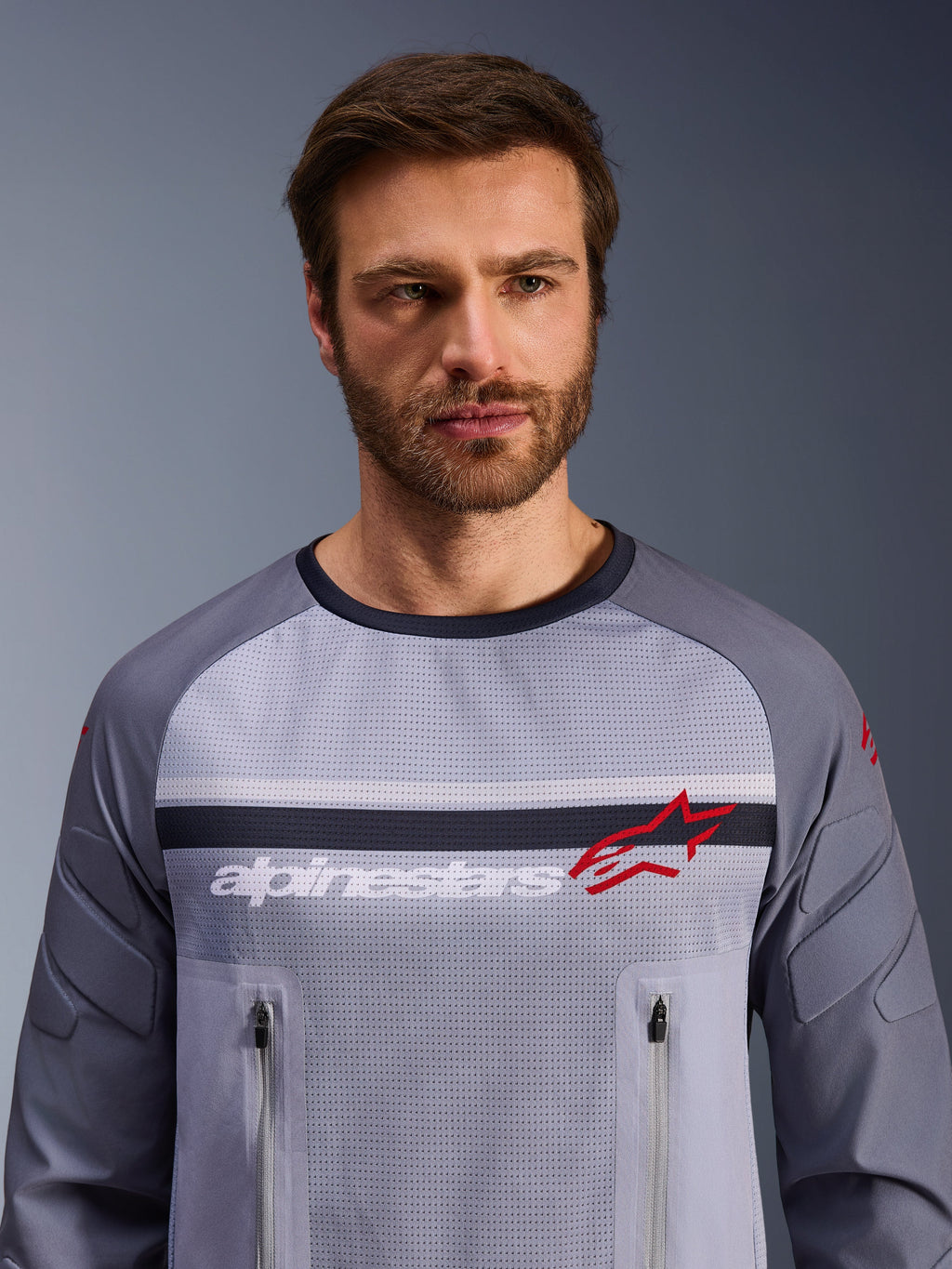 Alpinestars Maxdura Dual Jersey, Mid Gray och Dark Gray, bärs av en manlig modell, med mesh-torso för ventilation, dubbla bröstfickor med dragkedja, vit 'alpinestars'-text och röd stjärnlogotyp, teknisk utrustning för off-road och äventyrskörning