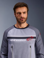 Alpinestars Maxdura Dual Jersey, Mid Gray och Dark Gray, bärs av en manlig modell, med mesh-torso för ventilation, dubbla bröstfickor med dragkedja, vit 'alpinestars'-text och röd stjärnlogotyp, teknisk utrustning för off-road och äventyrskörning