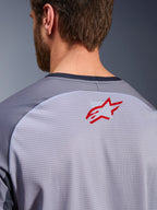 Alpinestars Maxdura Dual Jersey i mellangrå och mörkgrå, närbild på övre ryggen och kragen, liten röd Alpinestars stjärnlogotyp på ventilerande ljusgrått meshtyg med mörkgrå halskant, designad för äventyrskörning i terräng
