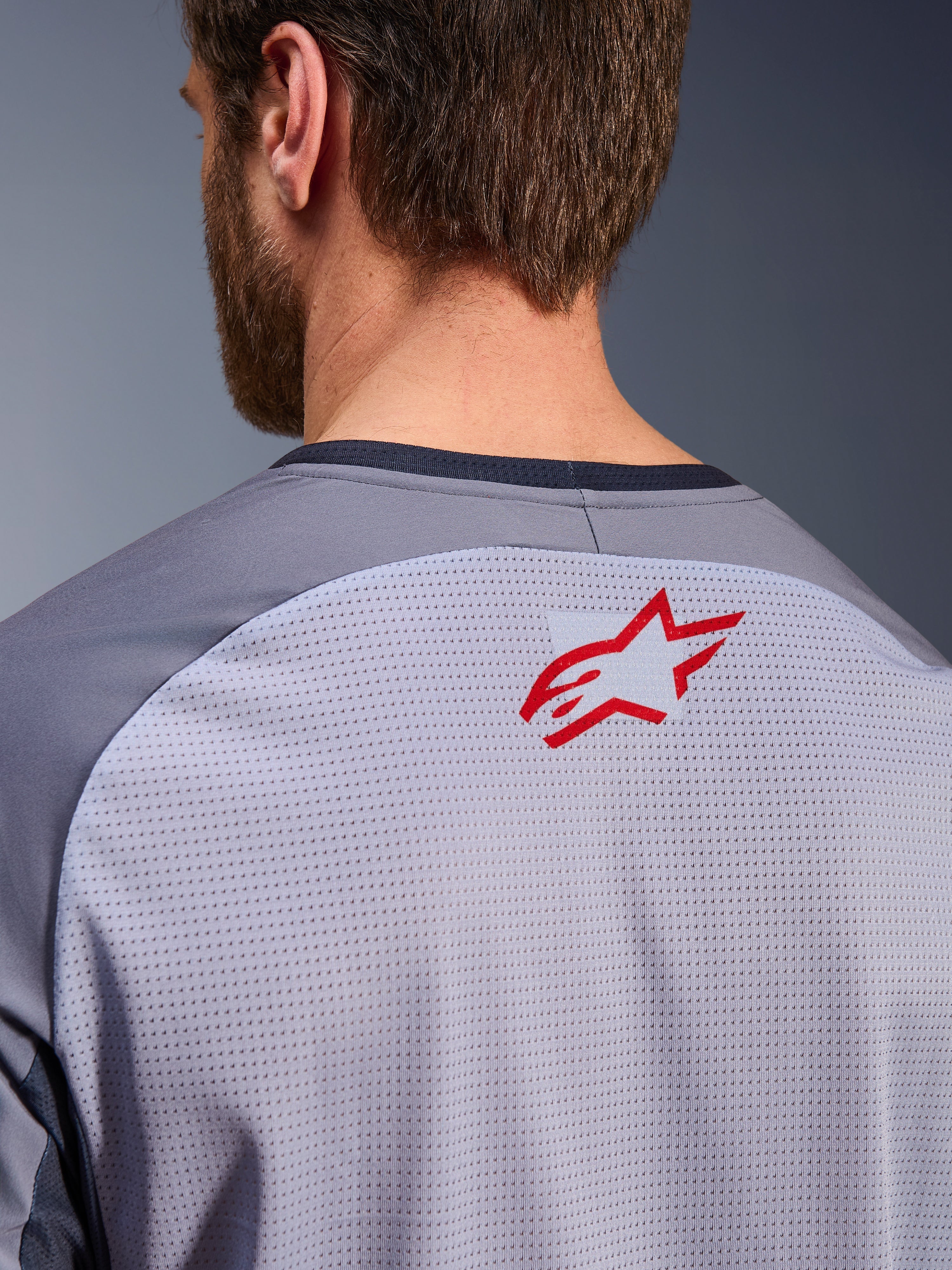 Alpinestars Maxdura Dual Jersey i mellangrå och mörkgrå, närbild på övre ryggen och kragen, liten röd Alpinestars stjärnlogotyp på ventilerande ljusgrått meshtyg med mörkgrå halskant, designad för äventyrskörning i terräng
