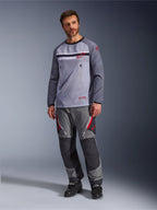 En man som bär Alpinestars Maxdura Dual Jersey i Mid Gray och Dark Gray, stylad med matchande grå och svarta adventurebyxor och svarta stövlar, med en ventilerande mesh-bål, bröstfickor med dragkedja och röda logotypdetaljer.