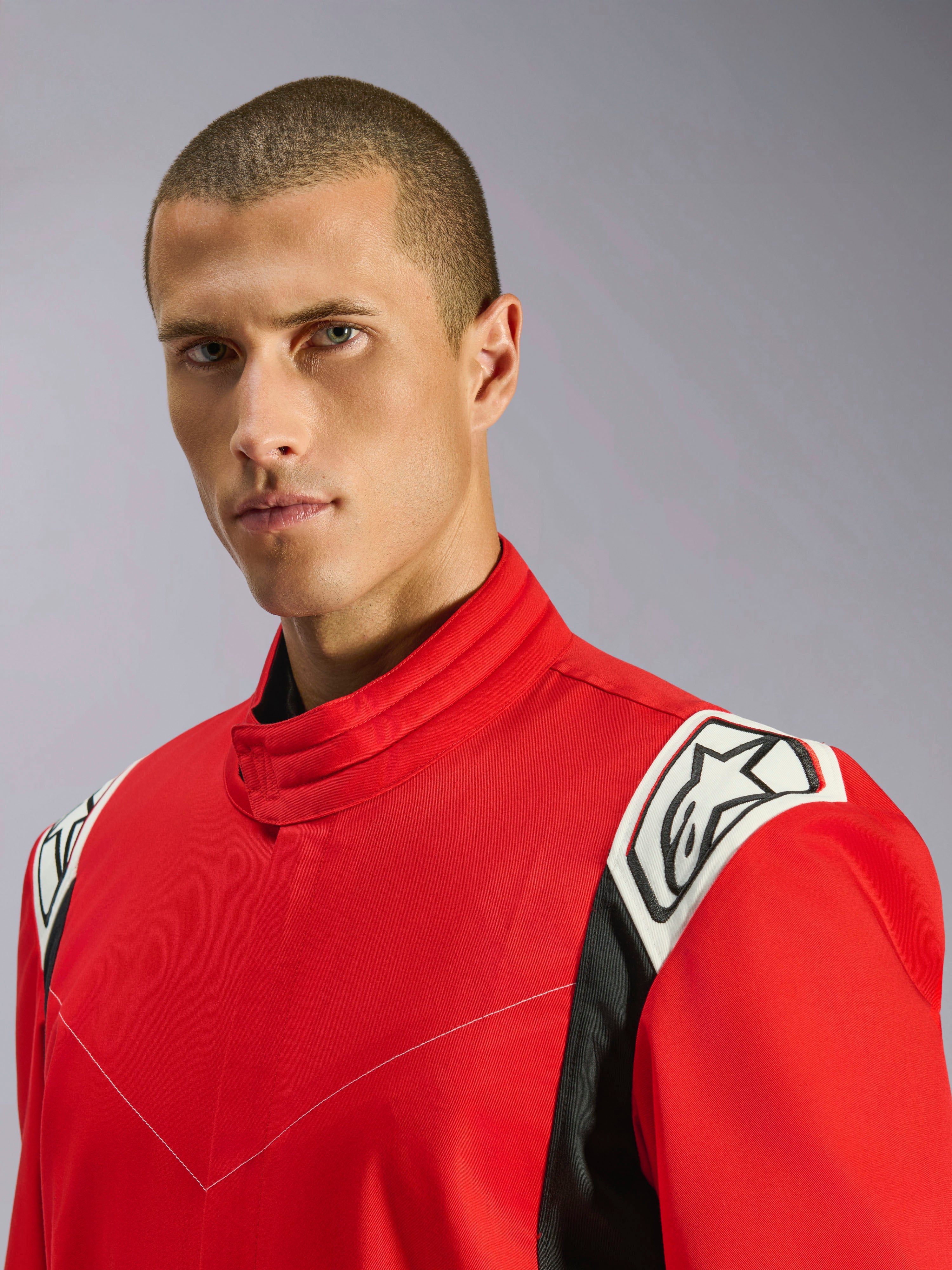 Alpinestars Kart Indoor V2-overall i rött, närbildsporträtt av en manlig modell som bär overallen, som framhäver den ergonomiska kragen och de vita och svarta axeldetaljerna med Alpinestars-logotypen.
