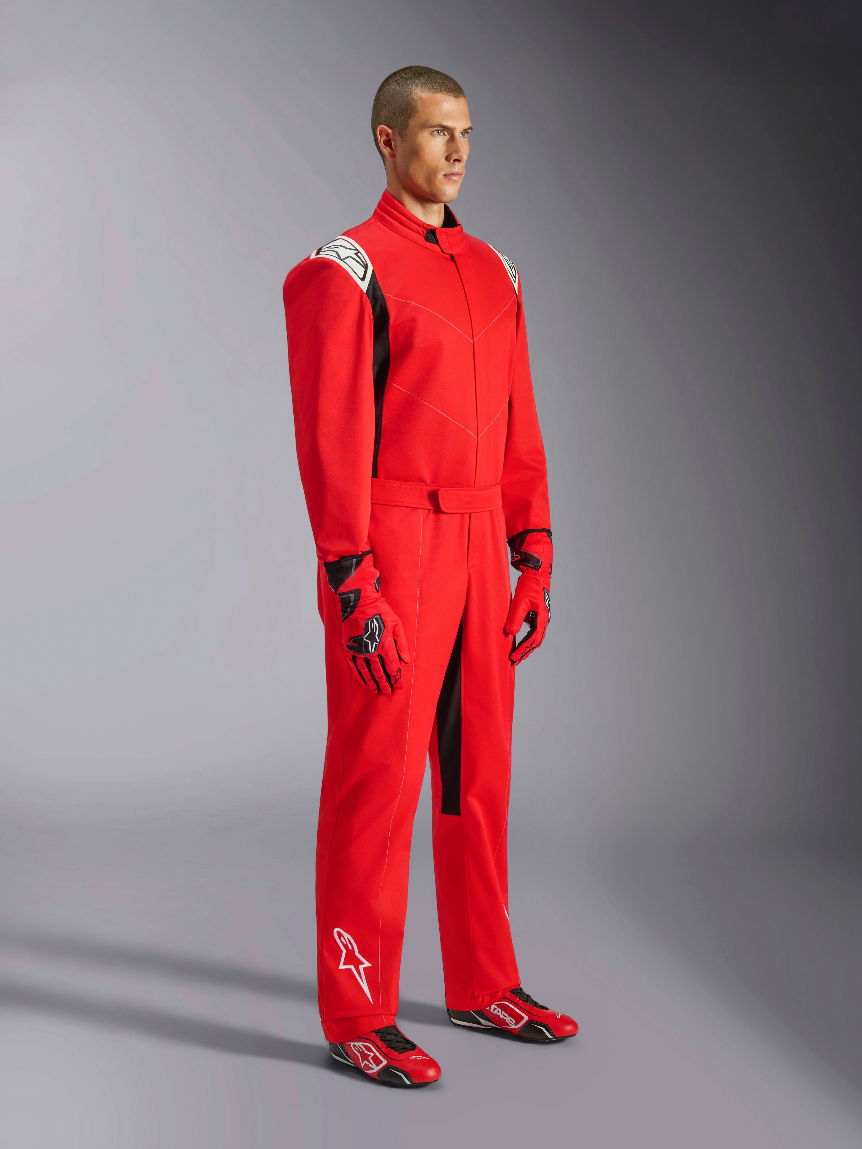 Alpinestars Kart Indoor V2-overall, röd kartingoverall, bärs av en modell med matchande röda och svarta handskar och skor, med vita logotyper på axlar och underben, svarta detaljer, designad för rekreationskarting och inomhusbanor