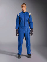 Manlig modell i Alpinestars Kart Indoor V2-overall i blått, helkroppsoverall för karting med vita stjärnlogotyper på axlar och smalben, vita kontrastsömmar, elastiskt midjebälte, stylad med svarta racinghandskar och skor, designad för rekreationsbruk på bana