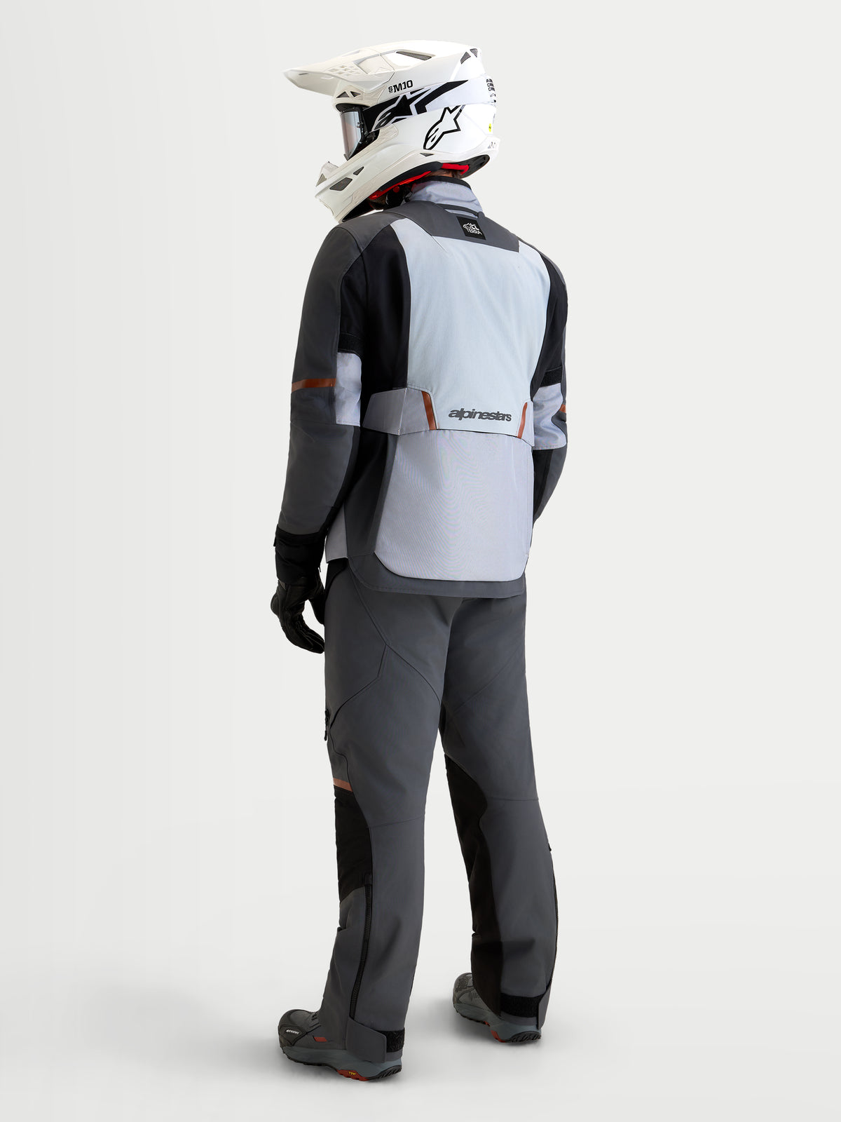 Alpinestars St-7 V2 2L Gore-Tex Gear Set, adventure touring motorcycle gear set, rear view of a model wearing grey, black, and light grey waterproof textile jacket and matching pants with a white helmet