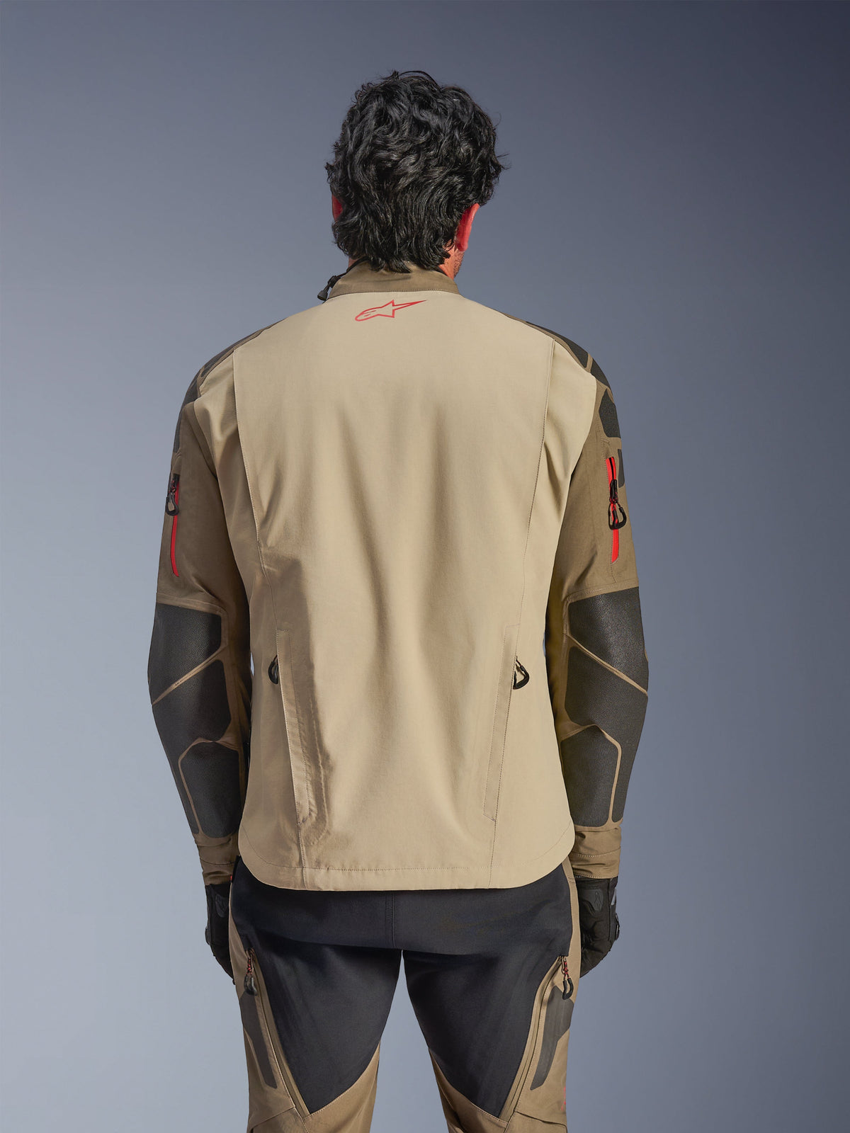 Alpinestars Nazca 3L GORE-TEX PRO-jacka, vy bakifrån, Walnut Rock Brown, äventyrsmotorcykeljacka med röd Astars-logotyp i nacken och röda dragkedjedetaljer på ärmarna, med Superfabric-förstärkningar på armbågarna.