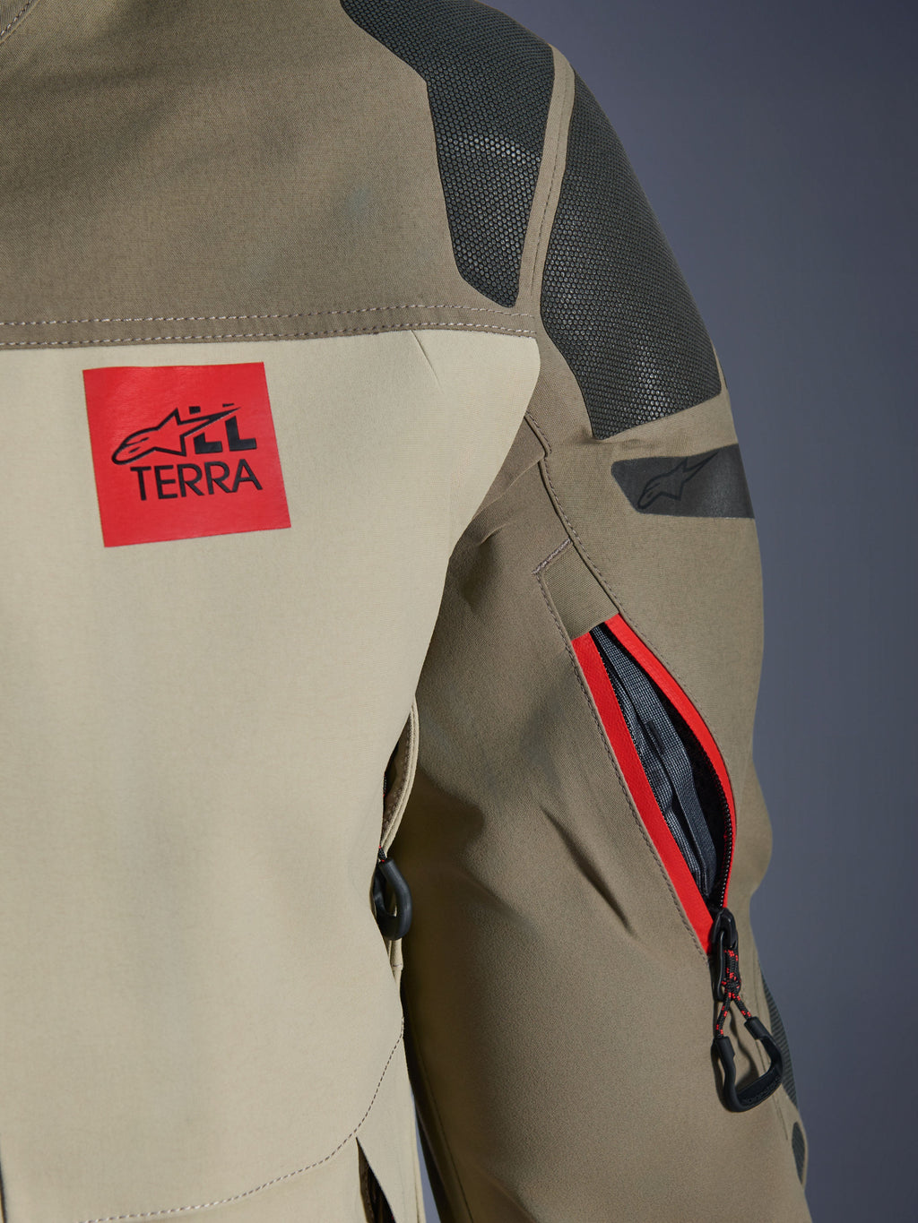 Alpinestars Nazca 3L GORE-TEX PRO-jacka, Walnut Rock Brown, detalj av baksidan av axel och ärm, röd 'ALL TERRA'-logotyp, texturerade svarta Superfabric-axelpaneler, dragkedjeförsedd ventilationsöppning på ärmen med röd kant, premium äventyrskläder för motorcykel.