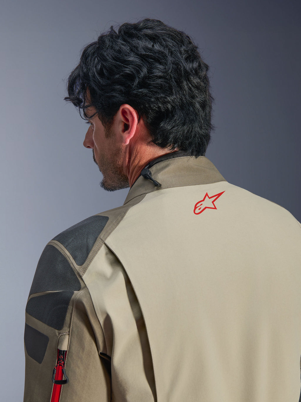 Alpinestars Nazca 3L GORE-TEX PRO-jacka, Walnut Rock Brown äventyrsjacka, närbild på rygg och axel, röd stjärnlogotyp på nacken, grå strukturerade förstärkningspaneler, slitstark textilkonstruktion för motorcykelkörning