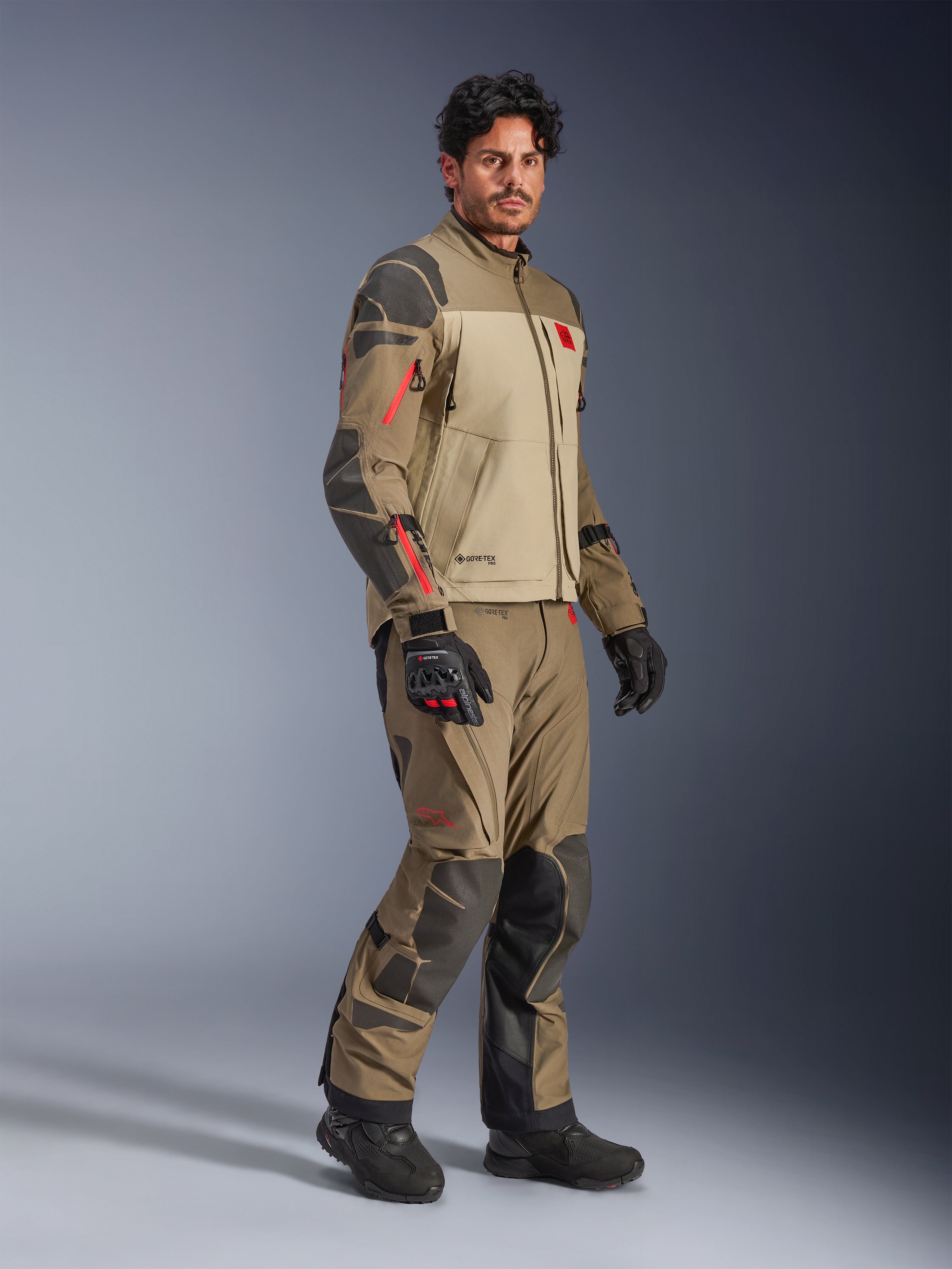 Alpinestars Nazca 3L GORE-TEX PRO-jacka, Walnut Rock Brown, äventyrsjacka för motorcykel buren med matchande byxor och svarta handskar, med mörkgrå förstärkningar, röda dragkedjedetaljer och ett högpresterande laminerat skal.