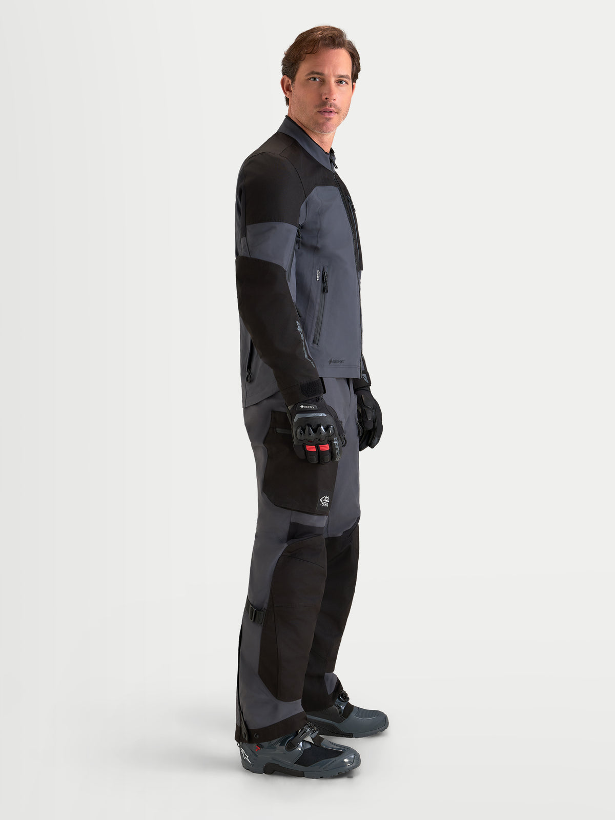 Alpinestars Arenis Gore-Tex Gear Set, äventyrsmotorcykeljacka och byxor för herr, svarta och mörkgrå, sidoprofilvy på modell som bär matchande äventyrsutrustning, vattentät GORE-TEX textilkonstruktion