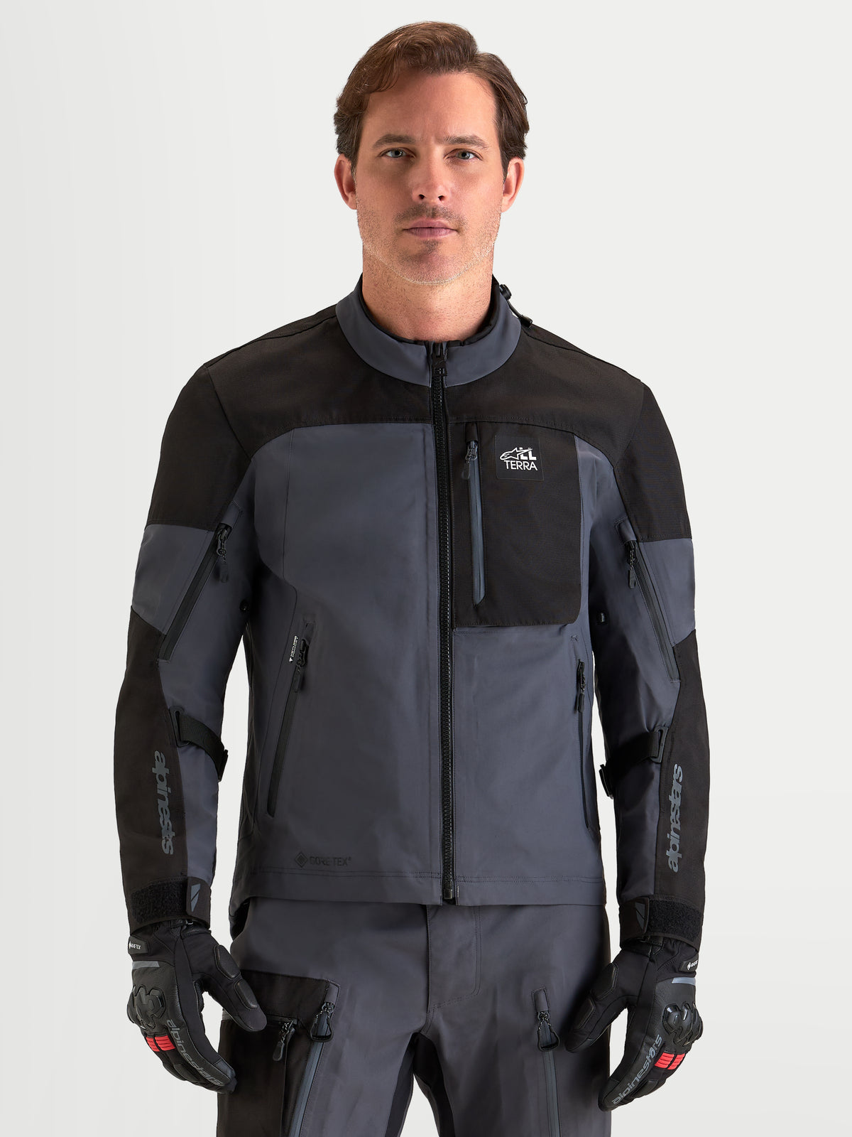 Alpinestars Arenis Gore-Tex jacka, äventyrsmotorcykeljacka för herr, svart och mörkgrå, framifrån på modell med matchande utrustning och handskar, AA-certifierad vattentät all-terrain-utrustning