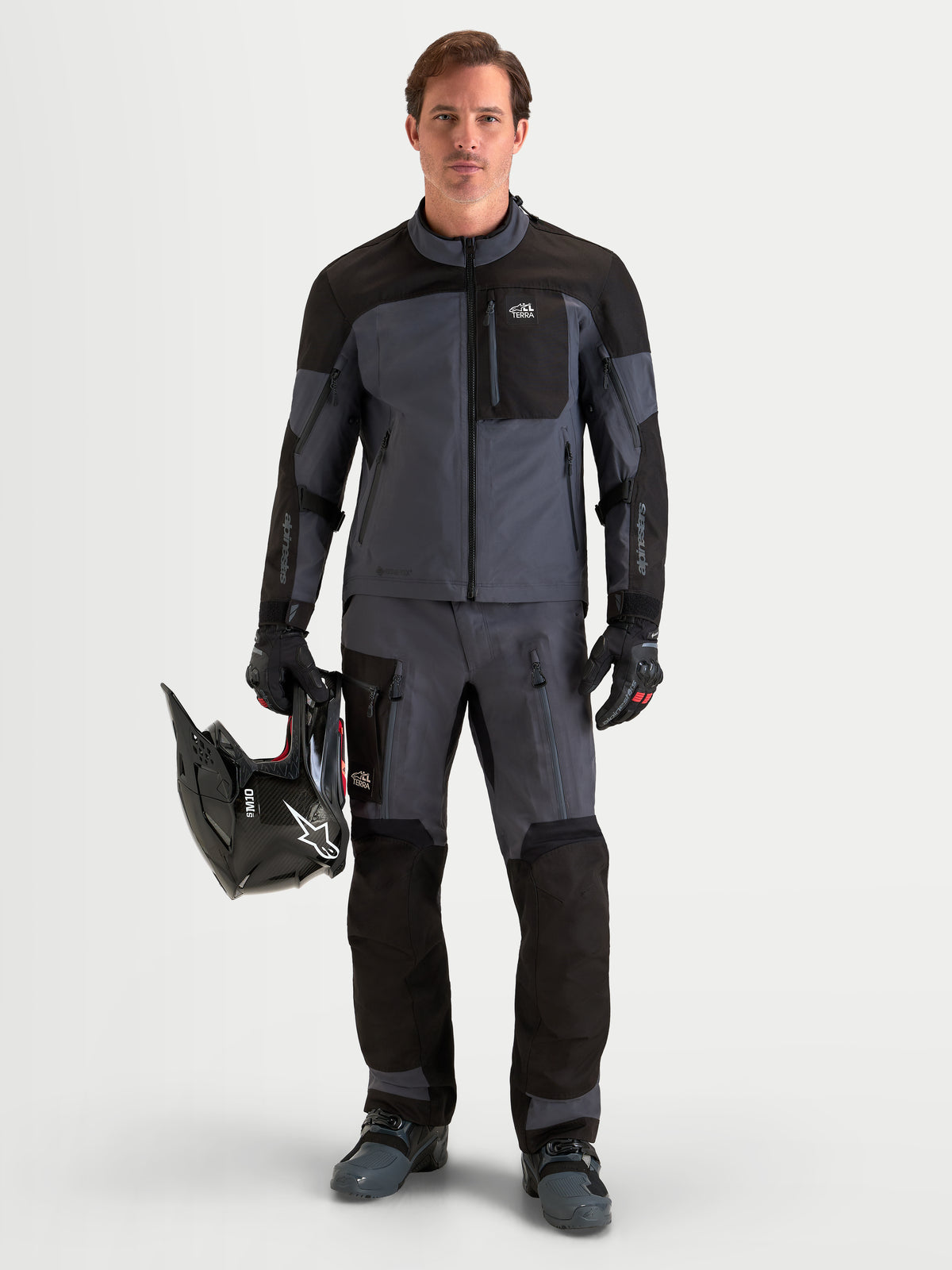 Alpinestars Arenis Gore-Tex gear set, äventyrsmotorcykeljacka och byxor för herr, svarta och mörka gråa, helkropps- och framifrånvy av en modell som står upp och håller en hjälm