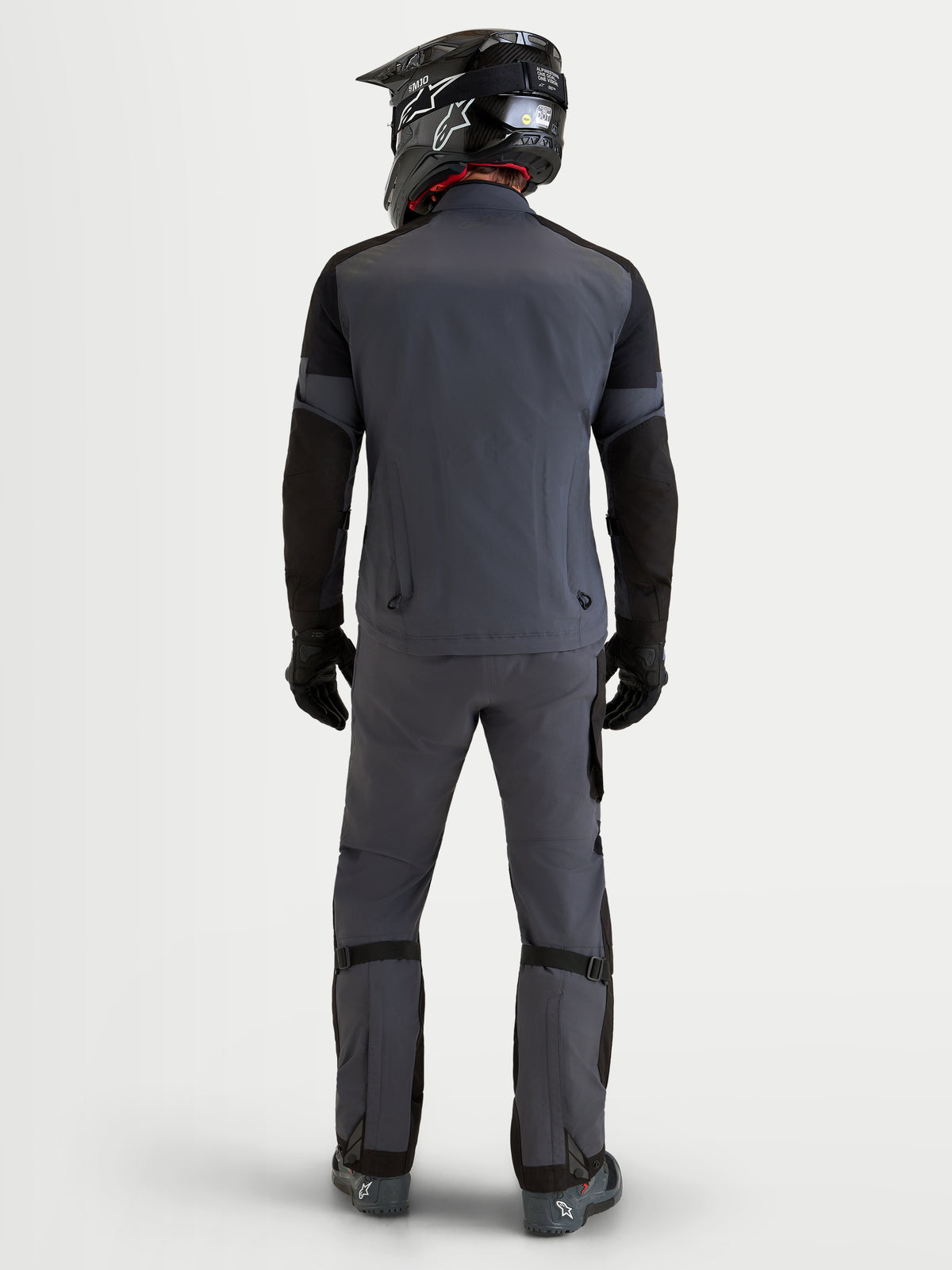 Alpinestars Arenis Gore-Tex Gear Set, äventyrsmotorcykeljacka och byxor för herr i mörkgrått och svart, vy bakifrån på en modell iklädd matchande hjälm och utrustning, vattentät GORE-TEX-utrustning för all terräng