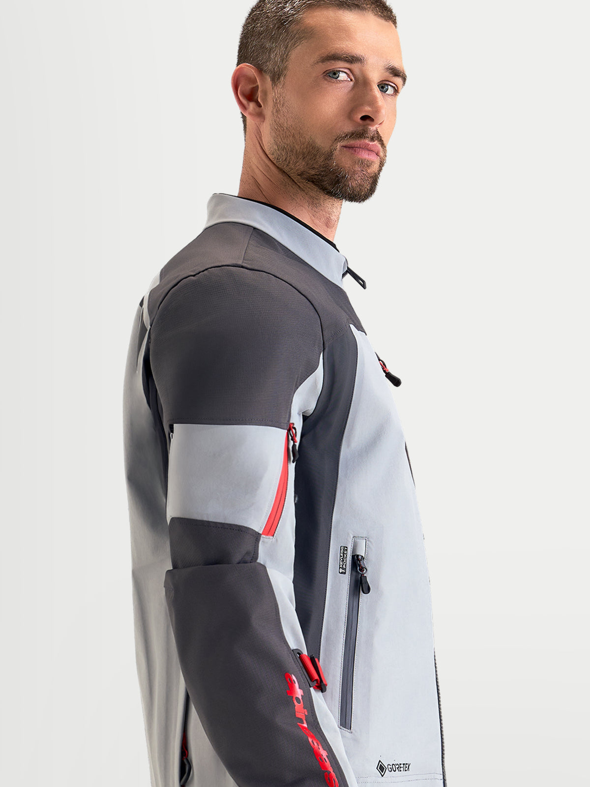 Alpinestars Arenis Gore-Tex jacka, äventyrsmotorcykeljacka för herr, mellanmörkgrå, mörkgrå och svart, sidoprofil som visar vattentät textilkonstruktion och ergonomisk krage på en modell