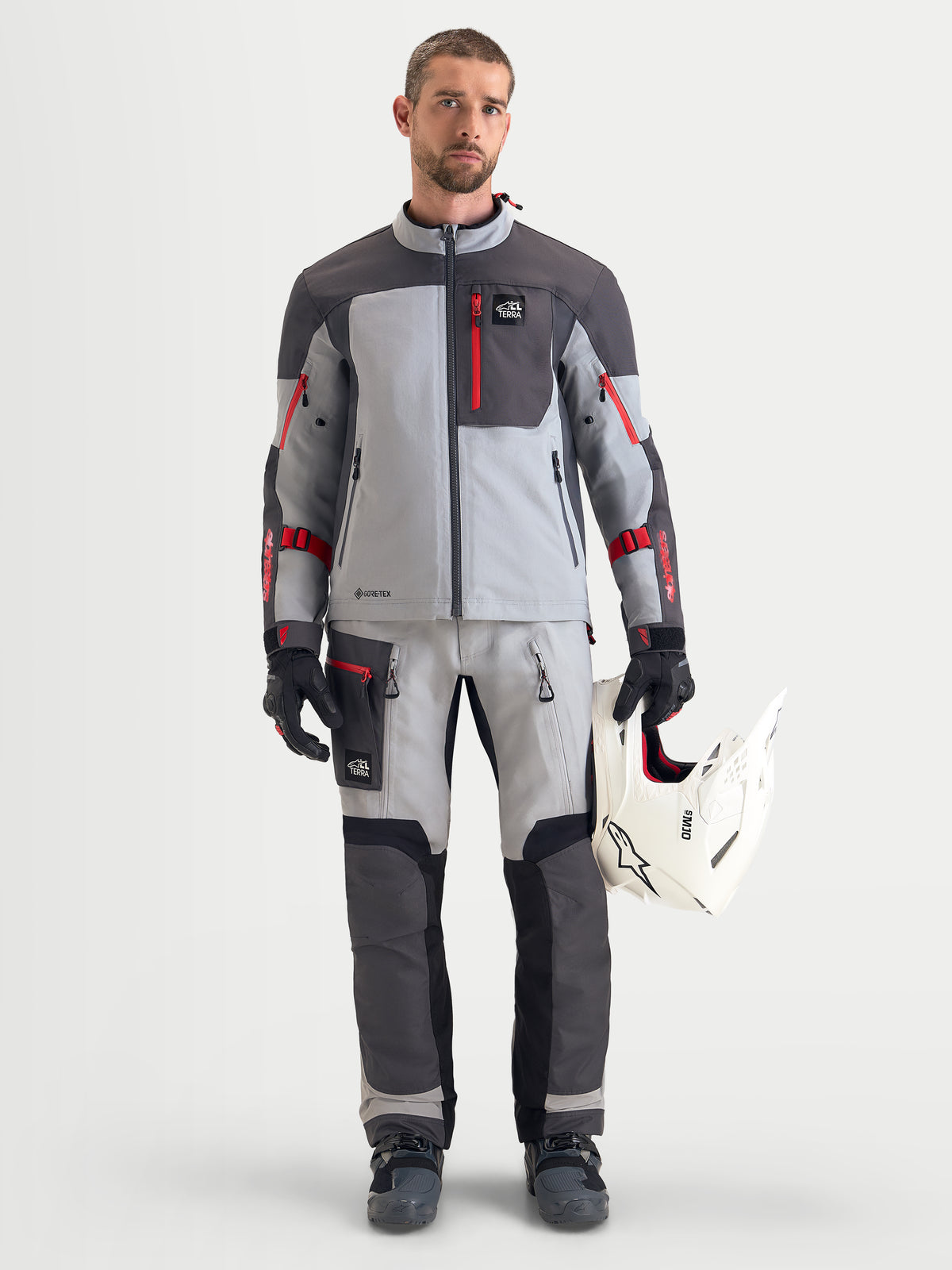 Alpinestars Arenis Gore-Tex jacka, äventyrsmotorcykeljacka för herr i mellanmörk grå, mörkgrå och svart, bars av en modell som håller i en vit hjälm