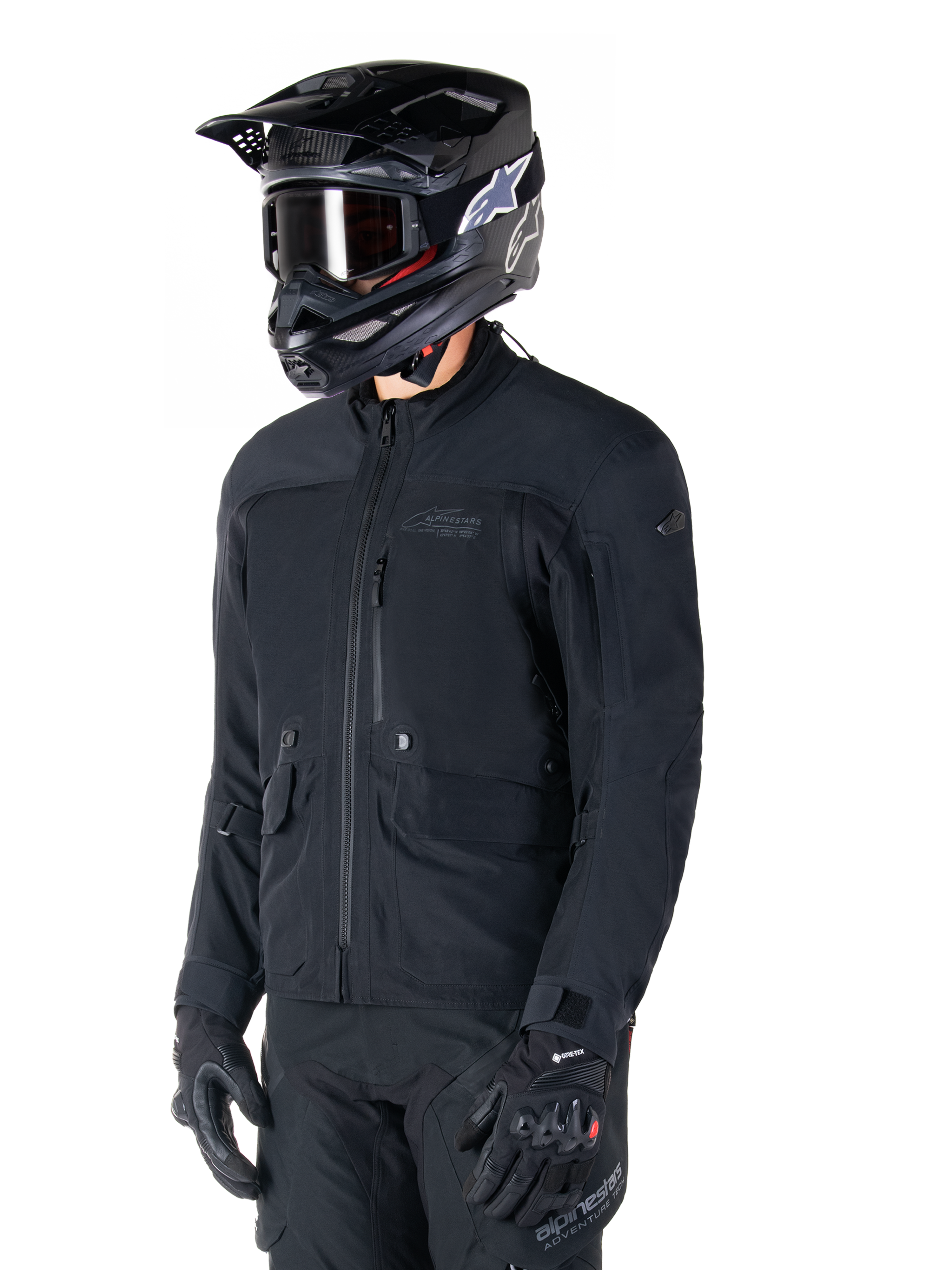 Alpinestars St-7 Prime GORE-TEX-jacka, svart motorcykeljacka, bärs av en förare med svart hjälm och goggles, stora bröstfickor i cargostil och ett laminerat vattentätt skal, premiumutrustning för adventure touring och pendling