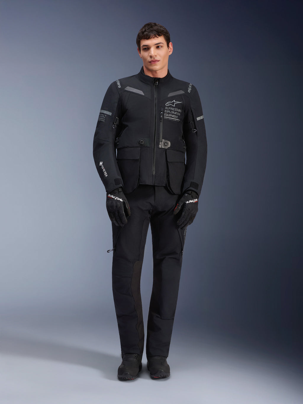 Alpinestars ST-7 2L GORE-TEX-jacka, motorcykeljacka för adventure-touring, svart och mörkgrå, bärs med matchande svarta körbyxor och handskar, med flera cargo-fickor, reflexdetaljer och Alpinestars Exploration Equipment-logotyp på bröstet, funktionell design för väg- och terrängkörning