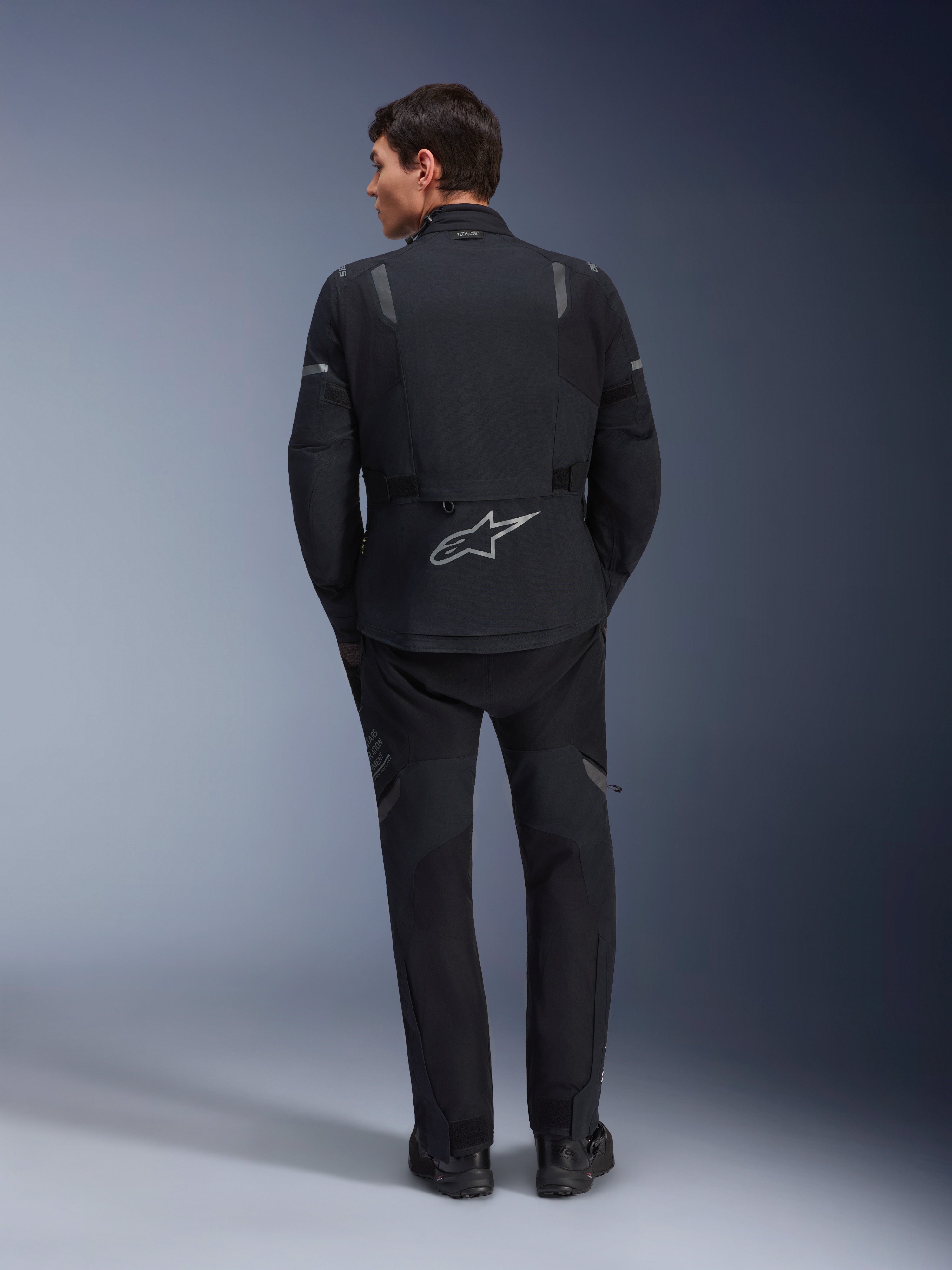 Alpinestars ST-7 2L GORE-TEX Jacket and matching ST-7 2L GORE-TEX Pants, Black and Dark Gray adventure motorcycle gear, rear view showing reflective Alpinestars logo on the jacket and technical textile construction.