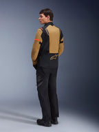 Alpinestars ST-7 2L GORE-TEX-jacka, äventyrsmotorcykeljacka, Gobi Brown och svart, sedd bakifrån på en modell som bär matchande mc-byxor och stövlar, med orangea detaljer på ärmarna, vattentätt laminerat skal och Alpinestars-logotyp, designad för touring och vägkörning