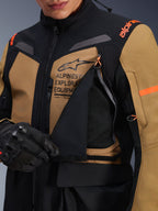 Alpinestars ST-7 2L GORE-TEX-jacka, motorcykeljacka för adventure touring, Gobi Brown och svart, närbild som visar den öppnade ventilationspanelen på bröstet som avslöjar ventilerande mesh, med Alpinestars Exploration Equipment-logotyp och orange detaljer.